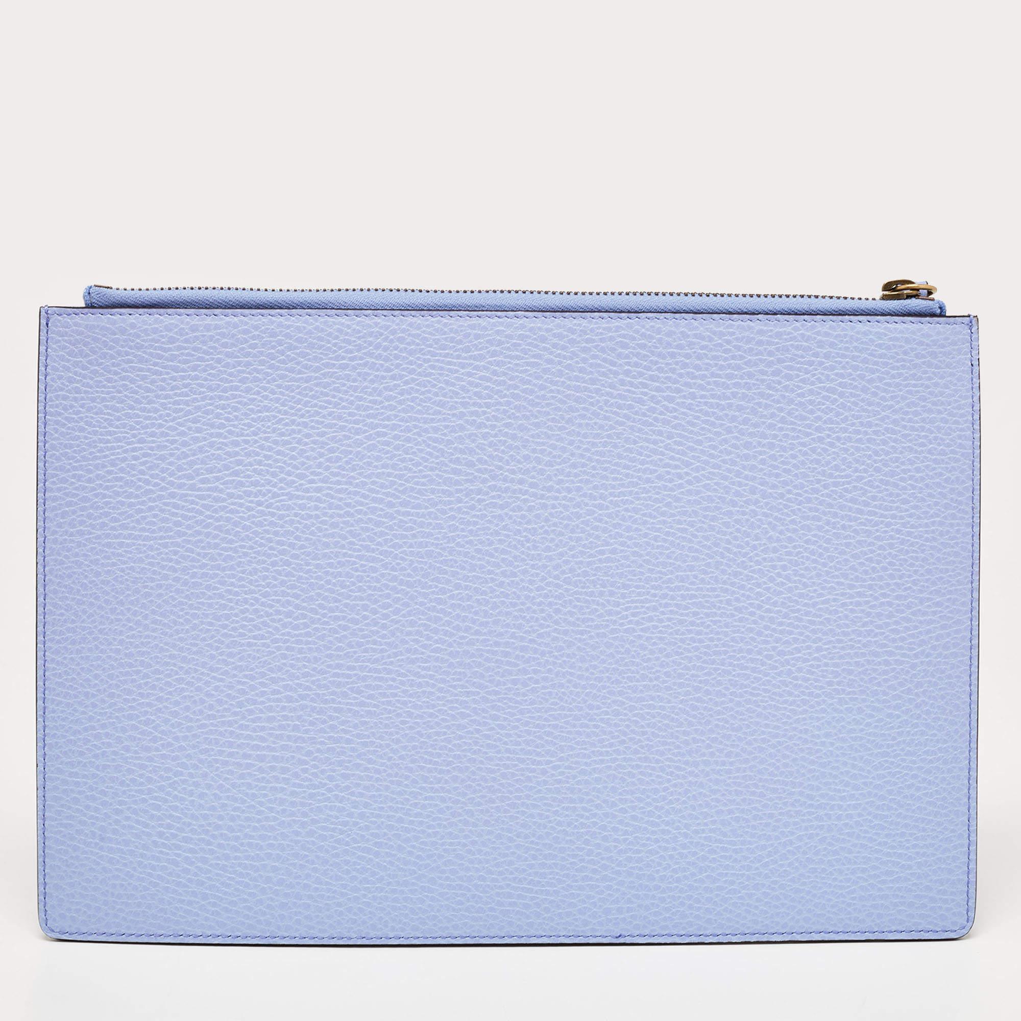 The Gucci clutch exudes elegance with its soft lavender hue and luxurious leather construction. It features a sleek, slim design perfect for carrying essentials. The charming cat motif adds a whimsical touch, making it a delightful accessory for any
