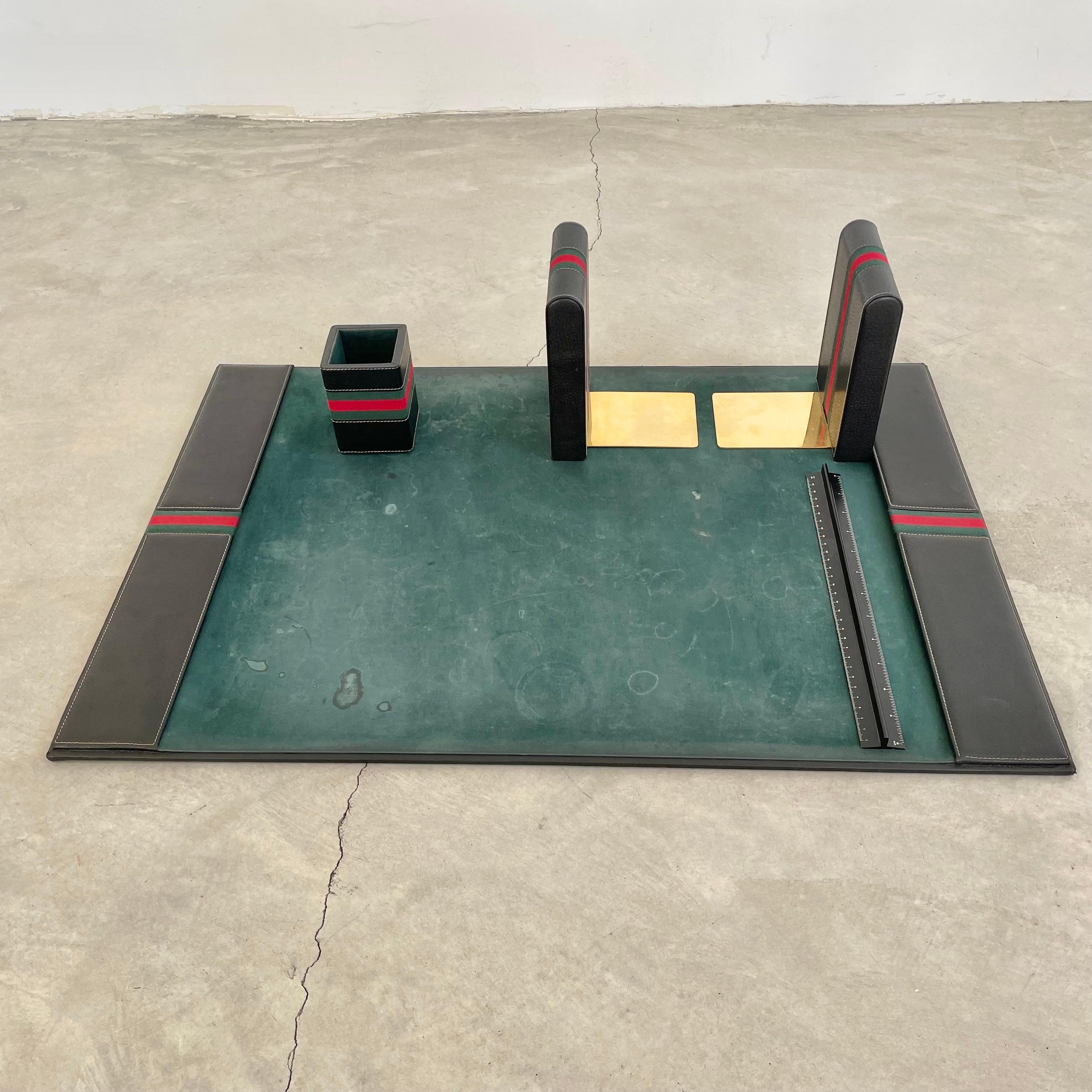 Beautiful Gucci desk set made of Black leather and emerald green velvet. Five pieces include: 2 Stunning leather and brass bookends, a pen holder, steel ruler in black and a large desk pad. Each piece is wrapped in the iconic red and green stripe