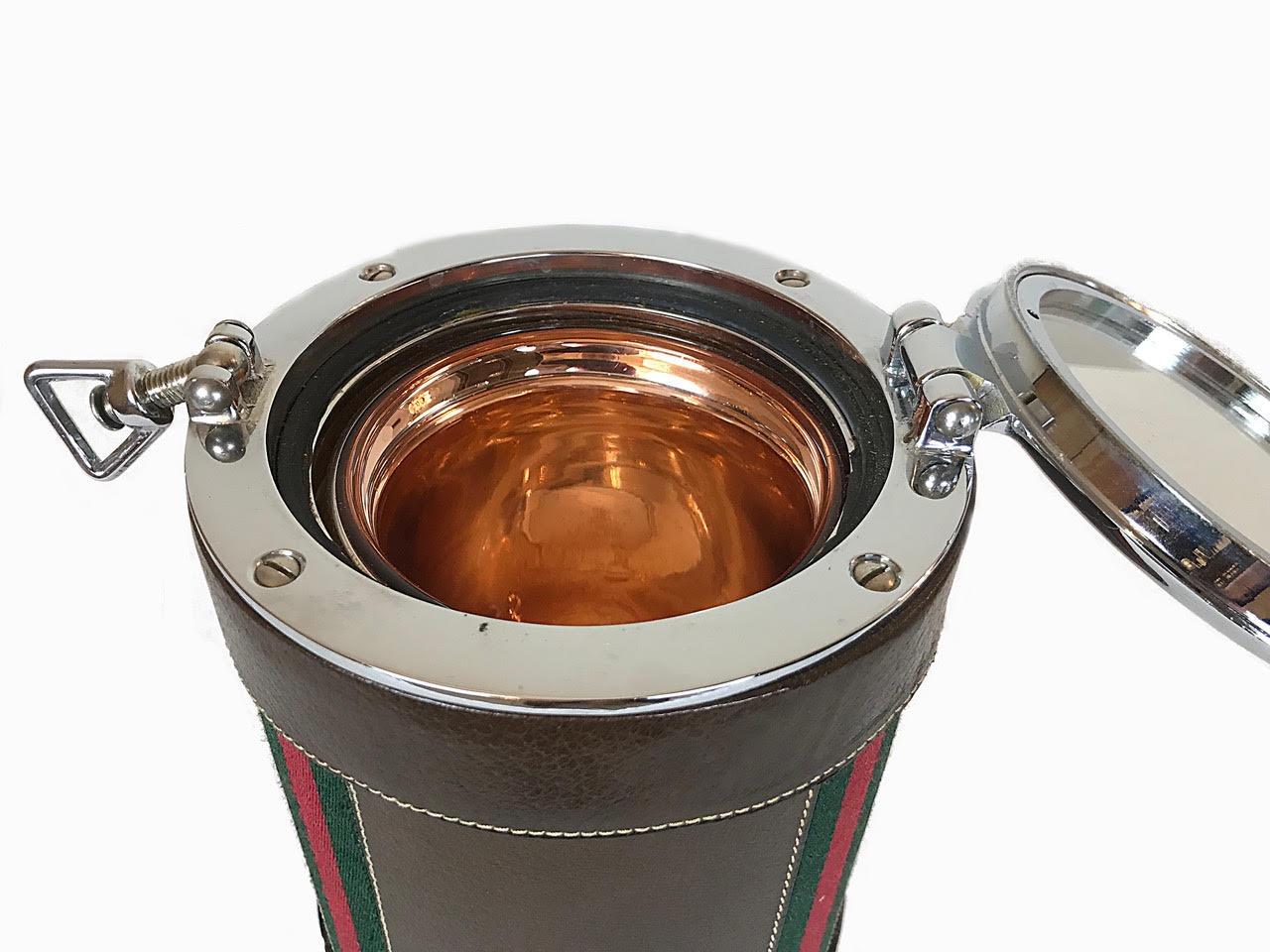 A fabulous ice bucket with lockable lid made for Gucci. The barrel is covered in leather with the stripes of the designer in green and red. There is a Gucci sticker on the bottom.