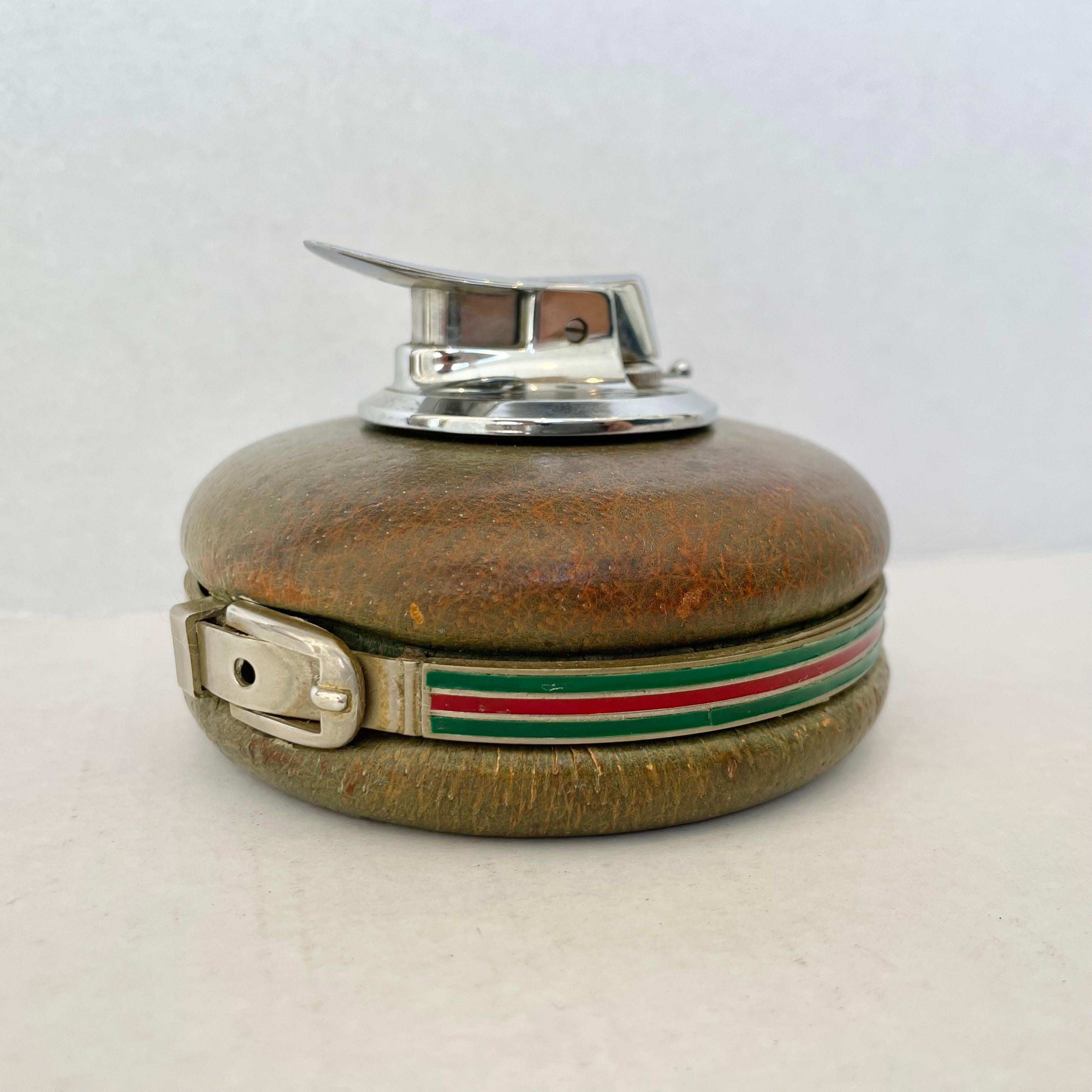 Elegant and rare Gucci table lighter with amazing details. Completely wrapped in leather which, at it's time of manufacture in the 50s, was green has now faded giving it a beautiful patina. The original leather color can still be seen on the base