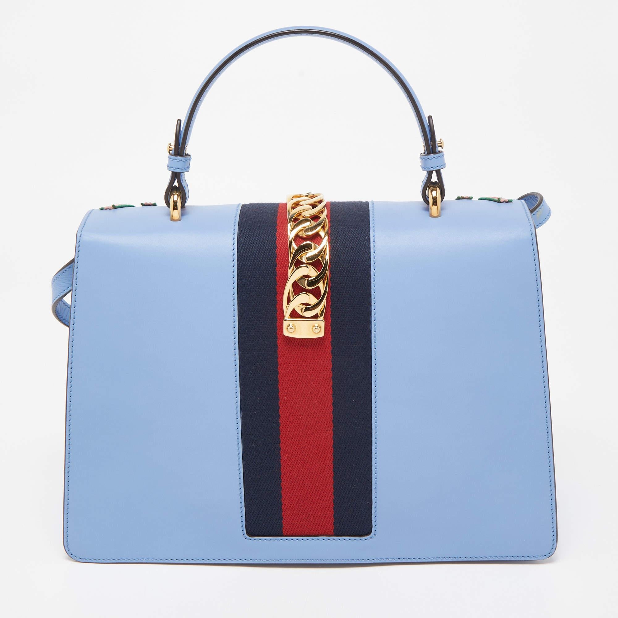 From the house of Gucci comes this gorgeous Sylvie bag that will perfectly complement all your outfits. It has been luxuriously crafted from blue leather and styled with floral embroidery on the front, a chain-web decorated flap, and a buckle lock
