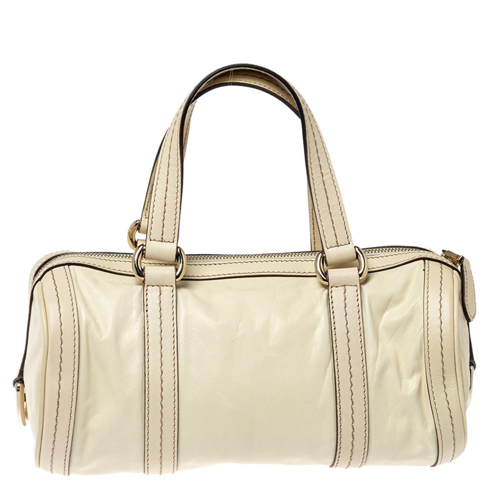 Diese Boston Tasche von Gucci ist aus cremefarbenem Leder gefertigt und mit einer Metallschleife auf der Vorderseite verziert. Sie verfügt über zwei Ledergriffe, und der Reißverschluss an der Oberseite gibt den Blick auf ein geräumiges,