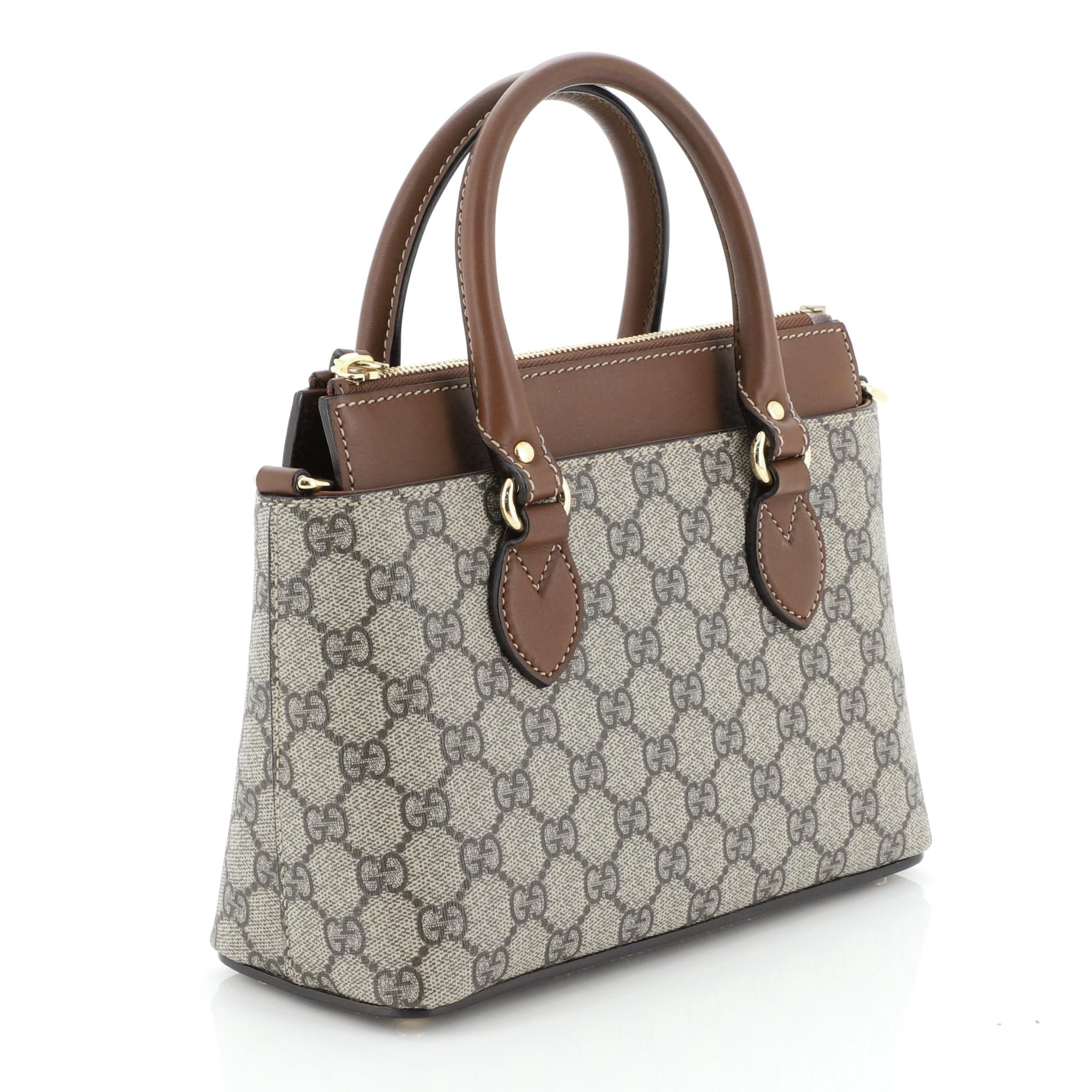 This Gucci Linea A Convertible Tote GG Coated Canvas Mini, crafted in brown GG coated canvas, features dual rolled leather handles, protective base studs, and gold-tone hardware. Its zip closure opens to a brown microfiber interior with slip