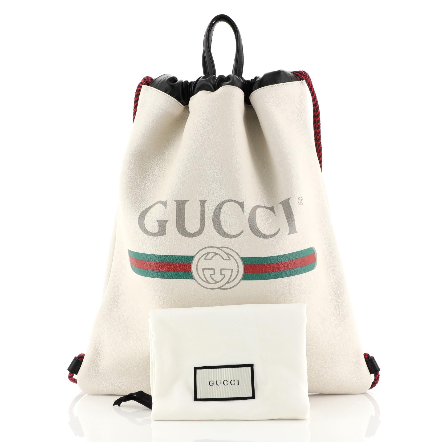 This Gucci Logo Drawstring Backpack Printed Leather Large, crafted in white printed leather, features dual leather top handles and rope straps that double function as a drawstring. Its drawstring closure opens to a white suede interior. 

Estimated