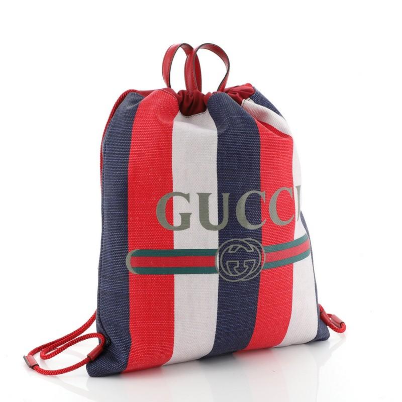 This Gucci Logo Drawstring Backpack Striped Raffia Large, crafted in white, blue, and red multicolor striped raffia, features dual leather top handles, rope straps that double function as a drawstring, and aged gold-tone hardware. Its drawstring