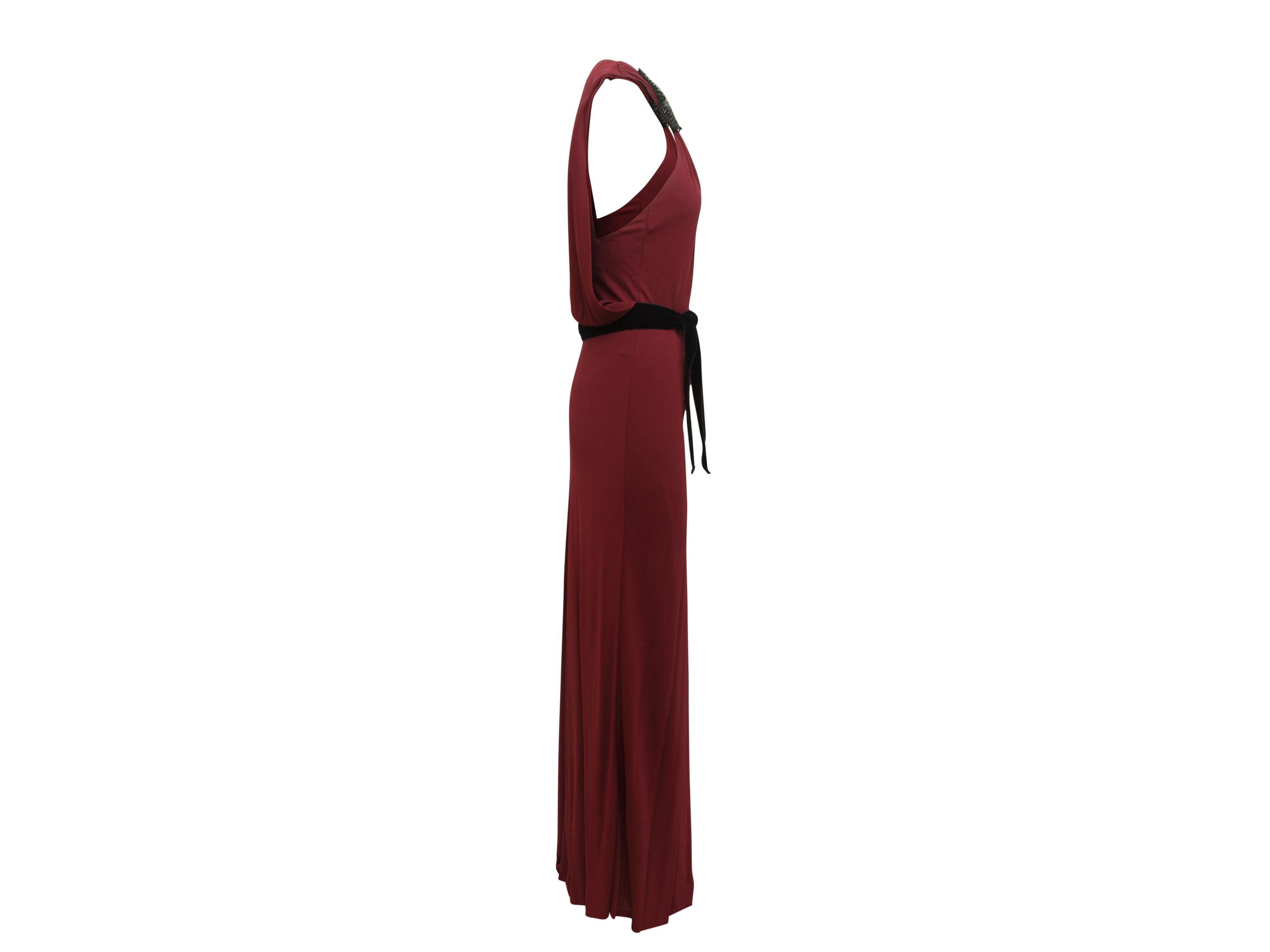 Product details:  Maroon Gucci column gown. The sleeveless gown has embellished wings appliqued at the neckline. The gown also has a black belt. It has a modified blouson waist. It has a one back button closure that creates a peek-a-boo effect at