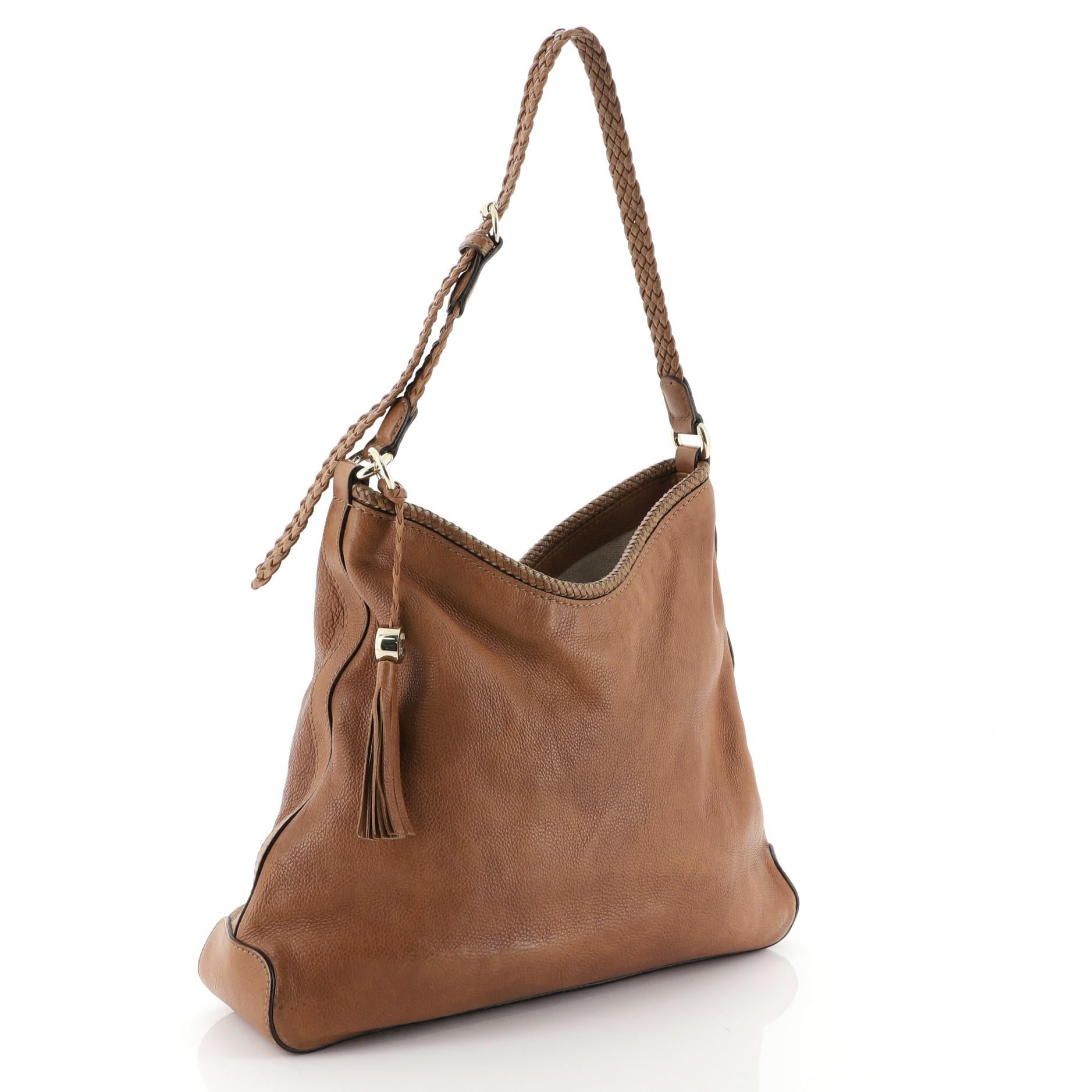 This Gucci Marrakech Hobo Leather Medium, crafted from brown leather with braided leather trims, features a looping shoulder strap, tassel detail, Gucci charms, and gold-tone hardware. Its magnetic snap closure opens to a neutral canvas interior