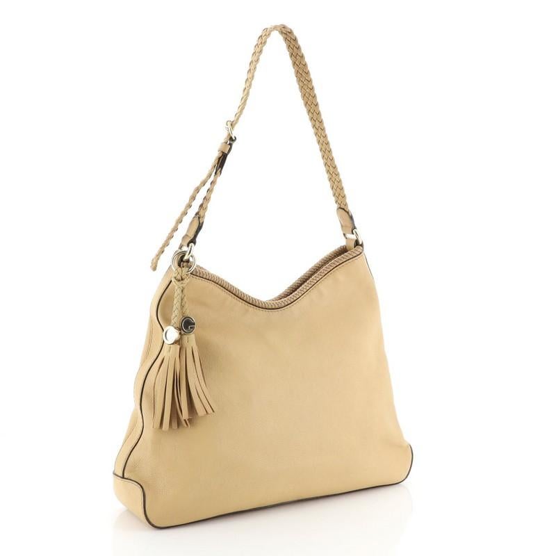 This Gucci Marrakech Hobo Leather Medium, crafted from neutral leather with braided leather trims, features a looping woven shoulder strap, Gucci charms and tassel ends and gold-tone hardware. Its magnetic snap closure opens to a neutral fabric