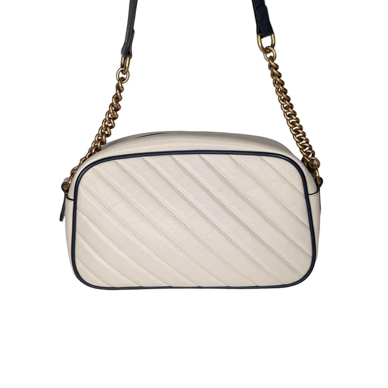 Gucci Vintage Effect Calfskin Matelasse Diagonal Small Torchon GG Marmont Chain Shoulder Bag in White and Blue. This stylish handbag is crafted of soft calfskin leather in off white with a diagonal quilt and navy blue leather accents. This shoulder