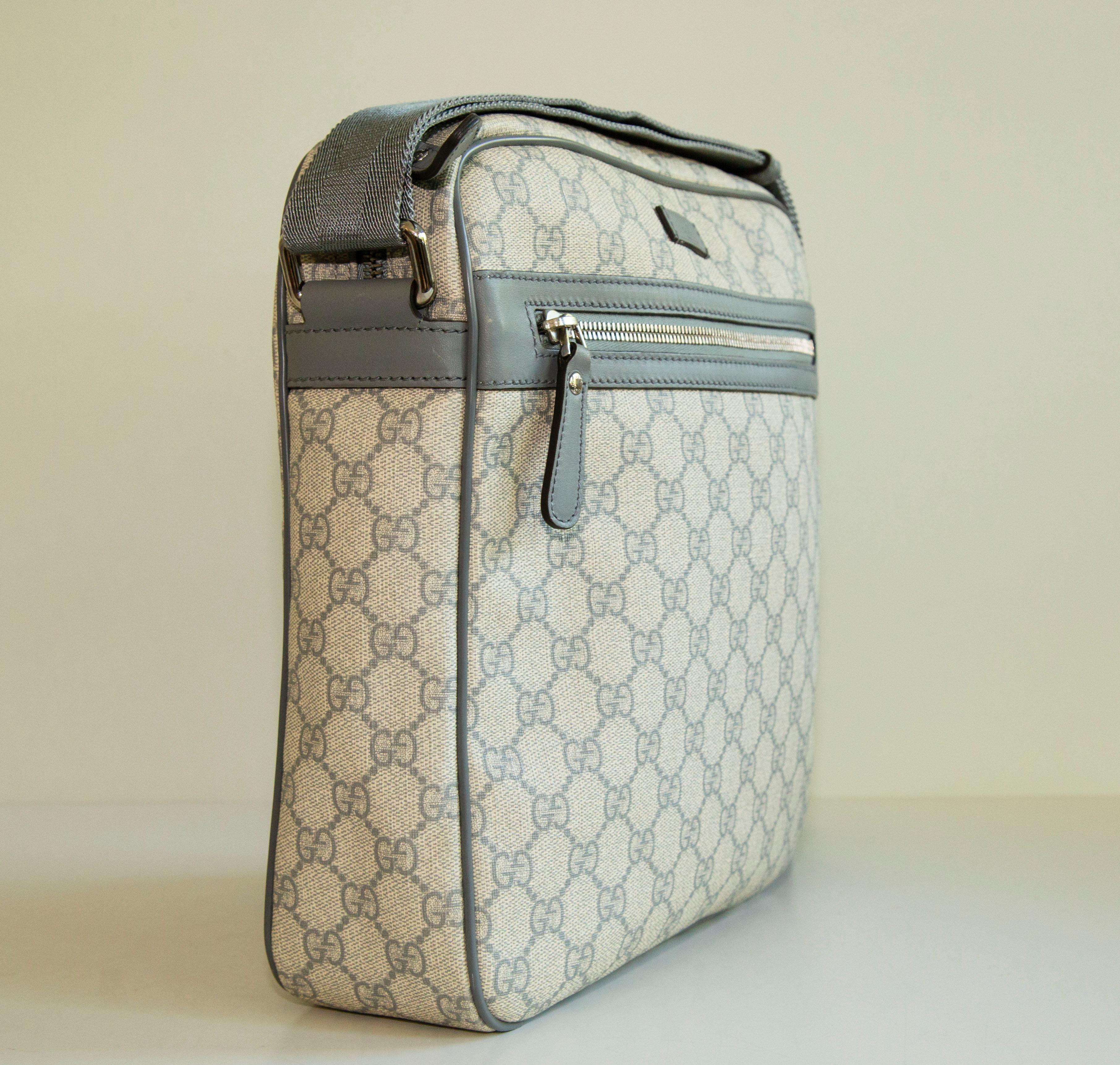 A Gucci messenger bag made of grey GG web coated canvas, grey leather trim,  with grey canvas shoulder strap and silver toned hardware. The interior is lined  with light beige canvas and next to the major compartment it features one side pocket. In