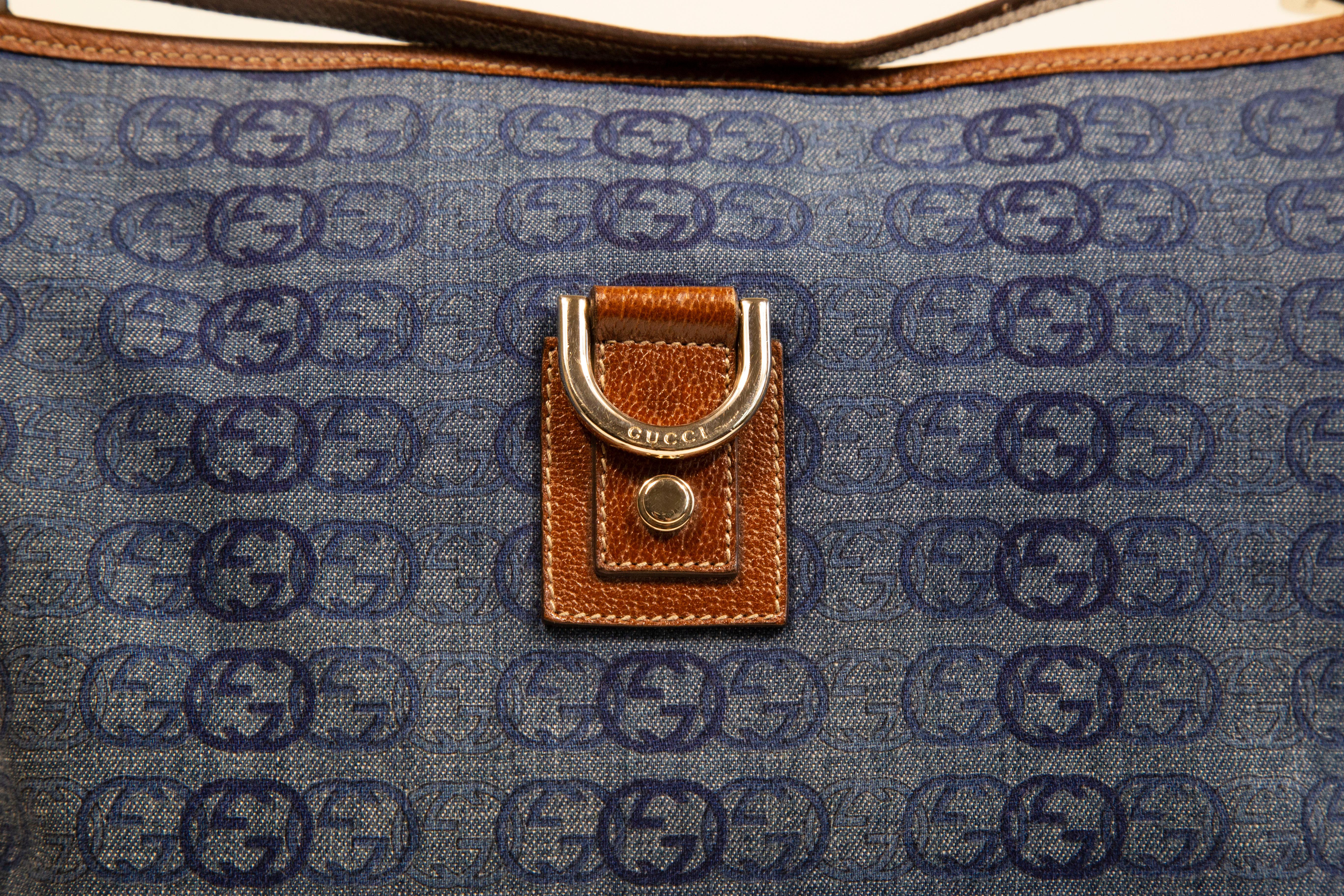 Un sac à main Gucci  en toile bleue/tissu jean avec motif GG imbriqué. Le sac est orné d'une bordure en cuir marron et de ferrures dorées. L'intérieur est doublé de tissu marron et comporte, à côté du compartiment principal, une poche pour téléphone