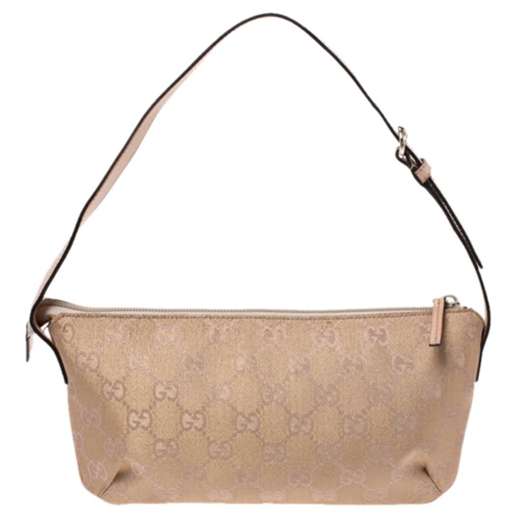 This pochette bag from Gucci is lovely. Crafted from the brand's signature GG canvas and leather, it comes in a beautiful shade of metallic beige. It is held by a single handle, features a zip closure that leads to a fabric interior with enough
