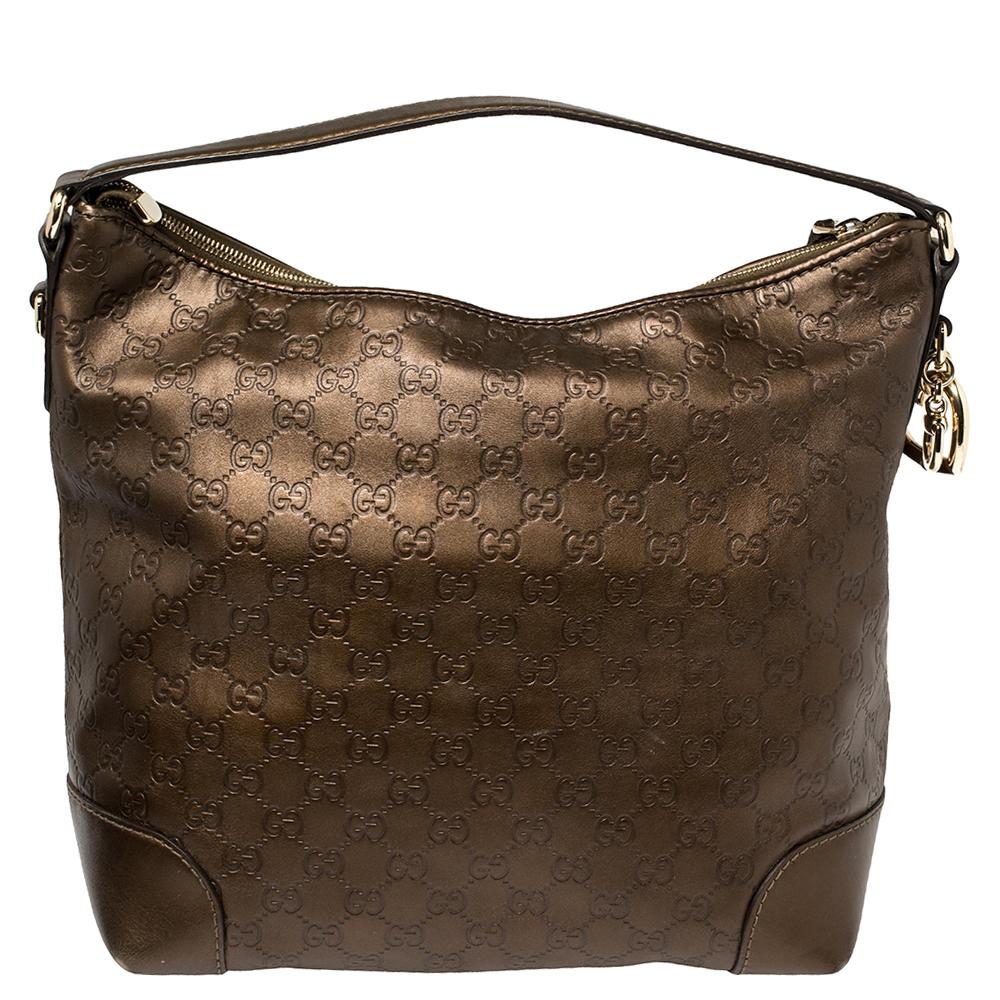 Glam up your daytime look with this large bronze metallic monogram Heart Bit hobo by Gucci. Crafted from quality leather, the handbag is accented with Gucci gold charms, leather trim, a comfortable single handle and gold-tone hardware. Its spacious
