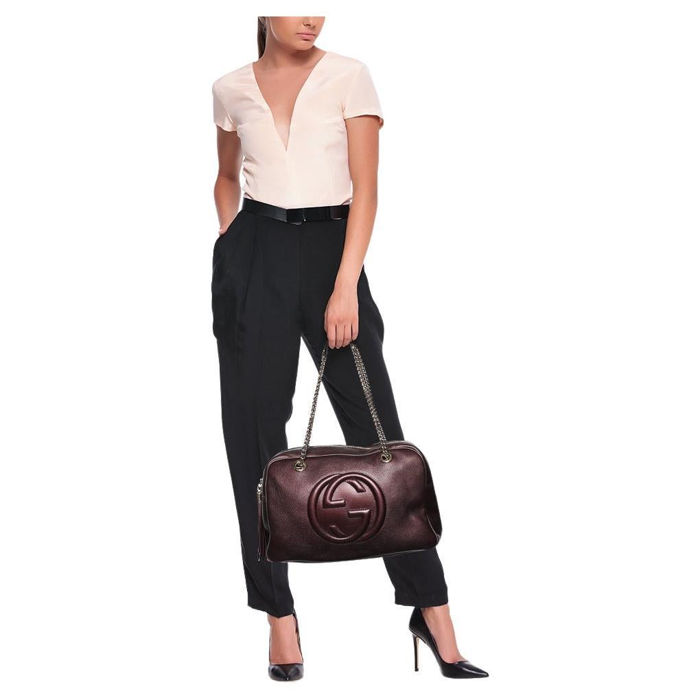 Gucci's expertise in crafting high-quality leather goods is evident through the creation of this piece. This Soho shoulder bag is designed using metallic-burgundy leather with an embossed logo motif highlighting the front. It is accented with