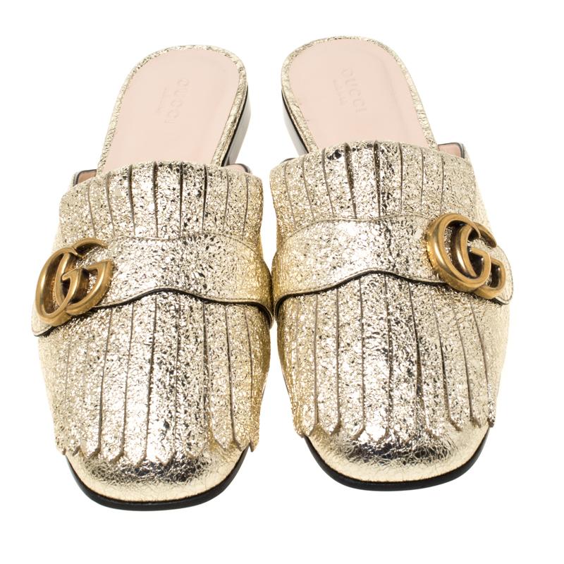 Dieses Paar Pantoletten von Gucci liegt voll im Trend und ist ein echter Hingucker. Sie wurden aus goldfarbenem Craquelé-Leder gefertigt und mit gefalteten Fransen und dem GG-Schriftzug der Marke auf dem Obermaterial gestylt. Bequeme Einlegesohlen