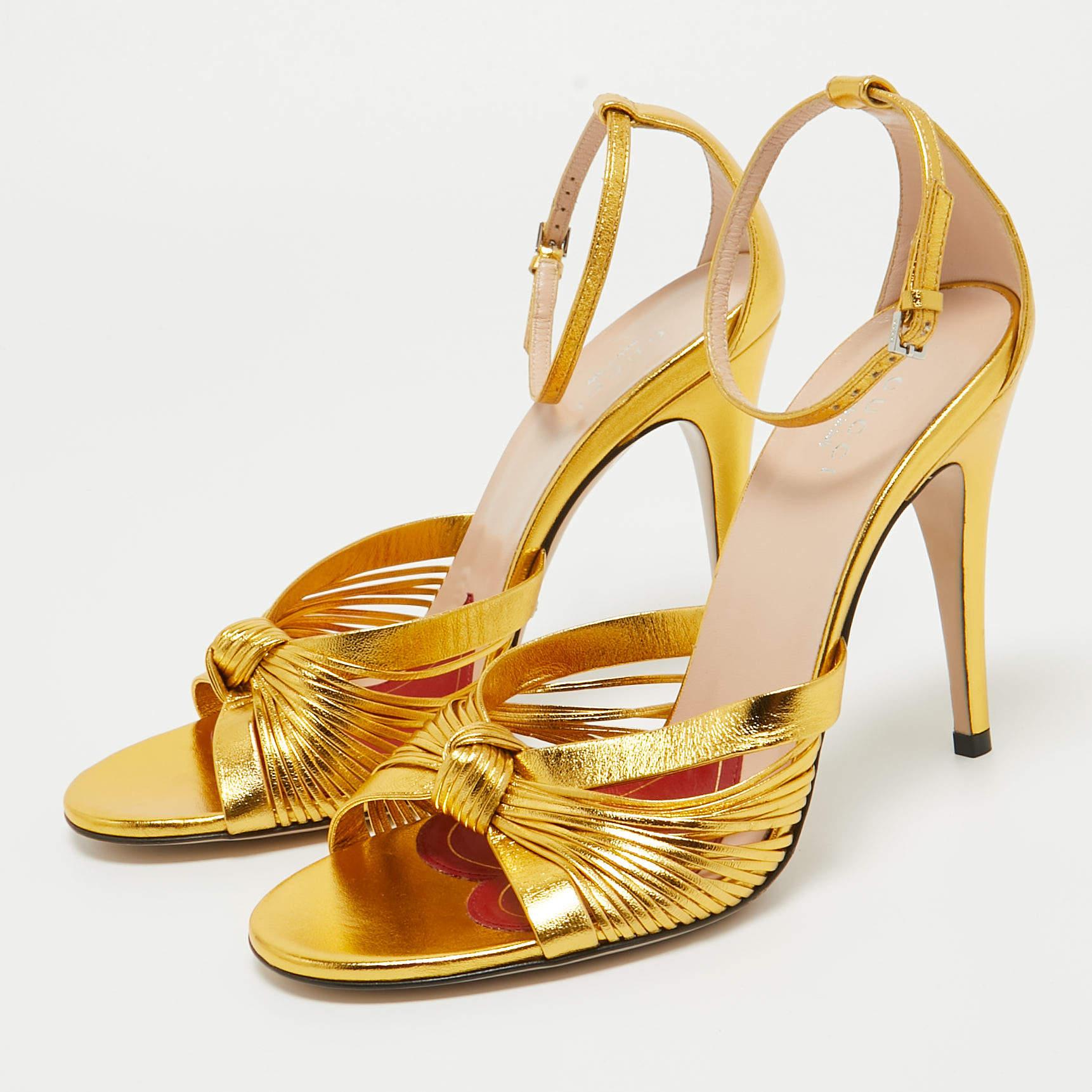 Beauty flows out of these sandals from Gucci! Crafted from metallic gold leather, these sandals have knotted gathering over the toes, open counters with ankle buckle straps and 10 cm heels to help you stand tall.

