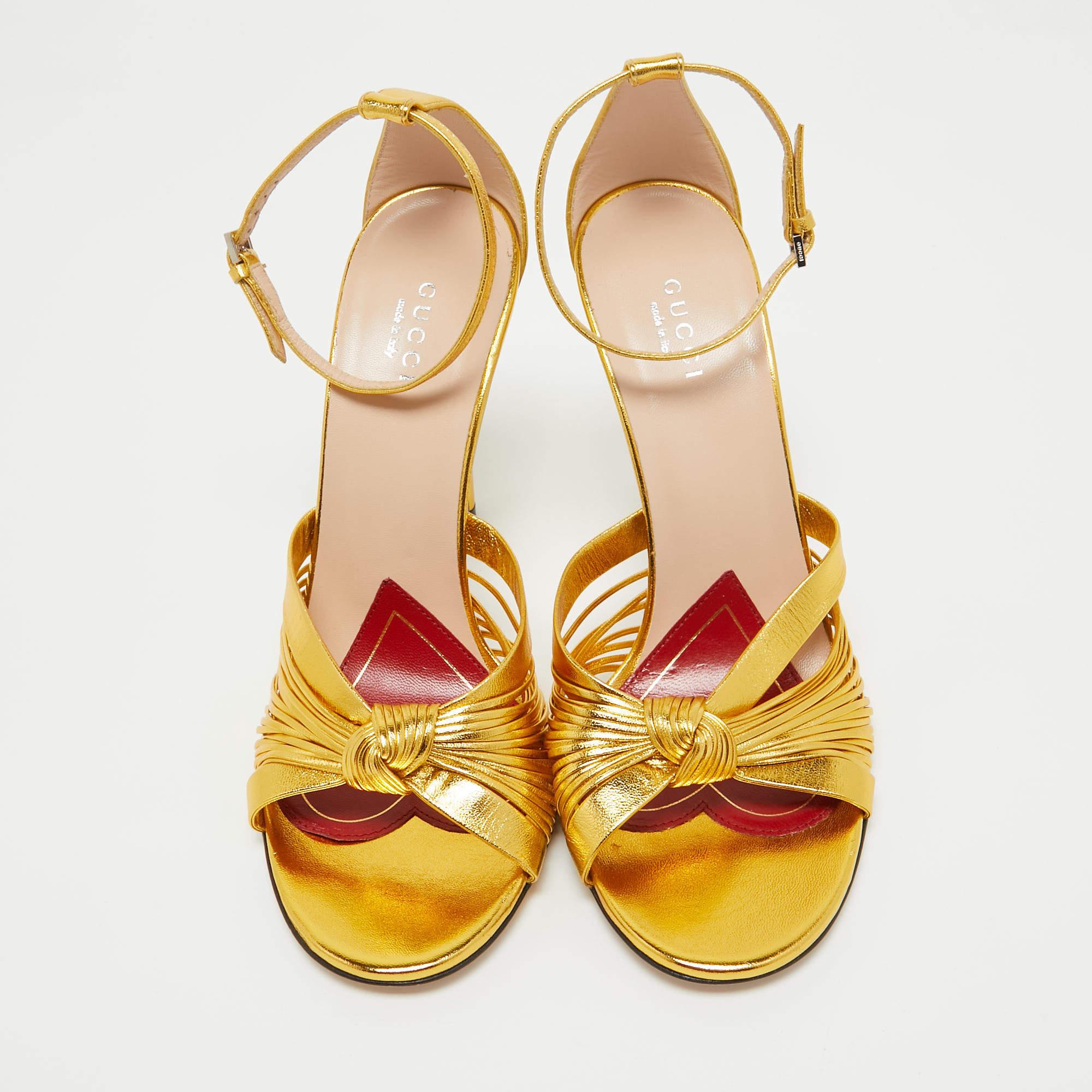 Beauty flows out of these sandals from Gucci! Crafted from metallic gold leather, these sandals have knotted gathering over the toes, open counters with ankle buckle straps and 10 cm heels to help you stand tall.

