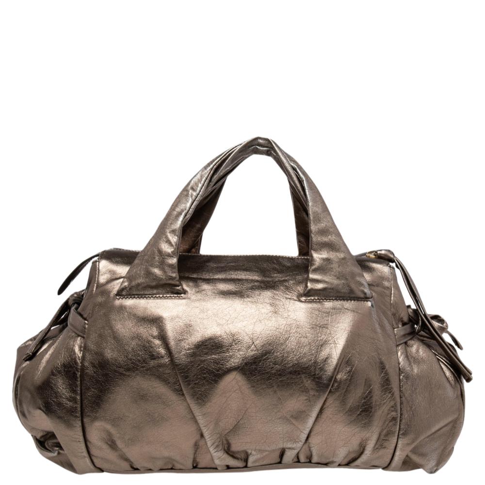 This Gucci Hysteria bag is built for everyday use. Crafted in Italy, it is made from leather and comes in a metallic gold hue. It has ties on the sides and dual handles for you to parade it. The nylon interior is spacious and is secured with zip