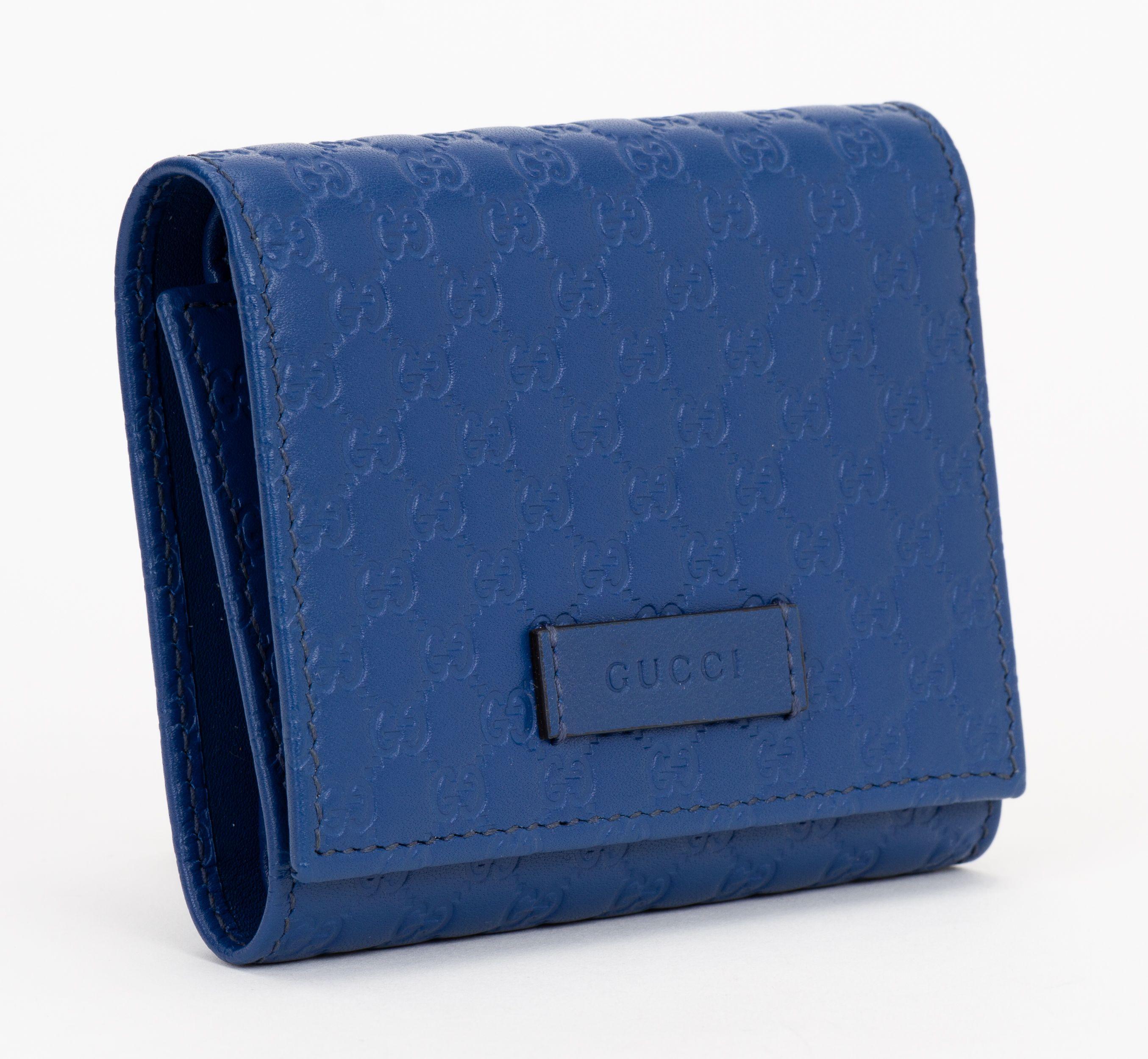Il portafoglio Gucci Microguccissima Flap Wallet in blu è realizzato in pelle blu con monogramma GG in rilievo e patta frontale. Si apre su un interno in pelle blu con una tasca con cerniera e, sul retro, presenta scomparti per carte e tasche