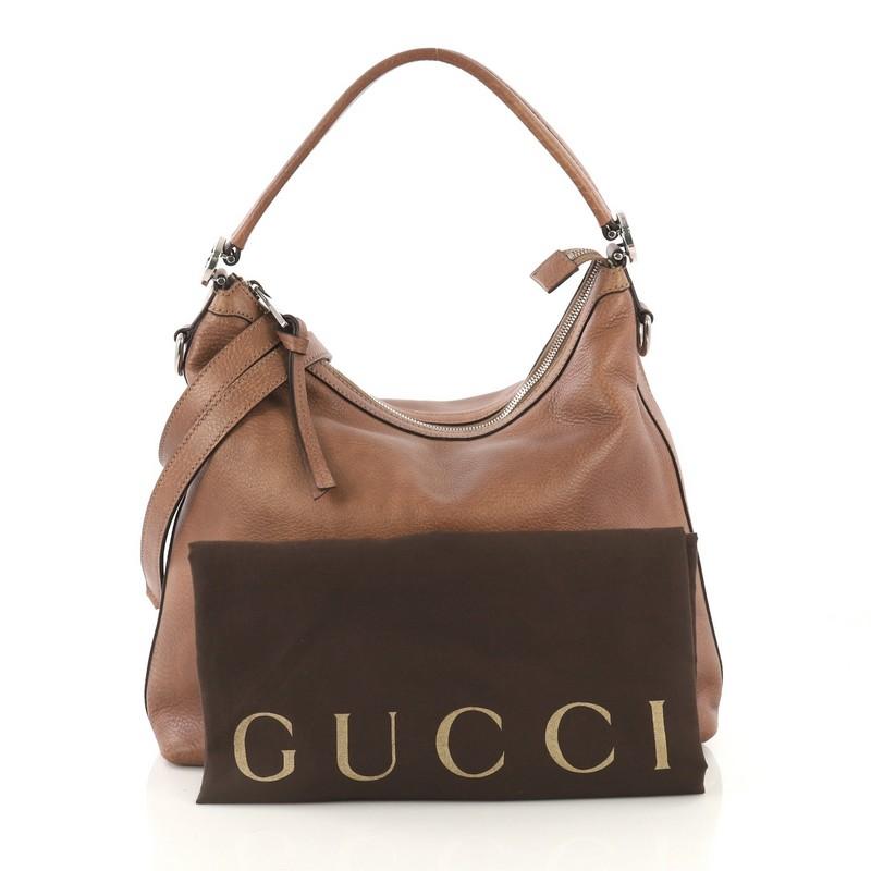 This Gucci Miss GG Hobo Leather Small, crafted from brown leather, features a flat leather shoulder strap, interlocking GG hardware on the side, and silver-tone hardware. Its zip closure opens to beige fabric interior with zip and slip pockets.