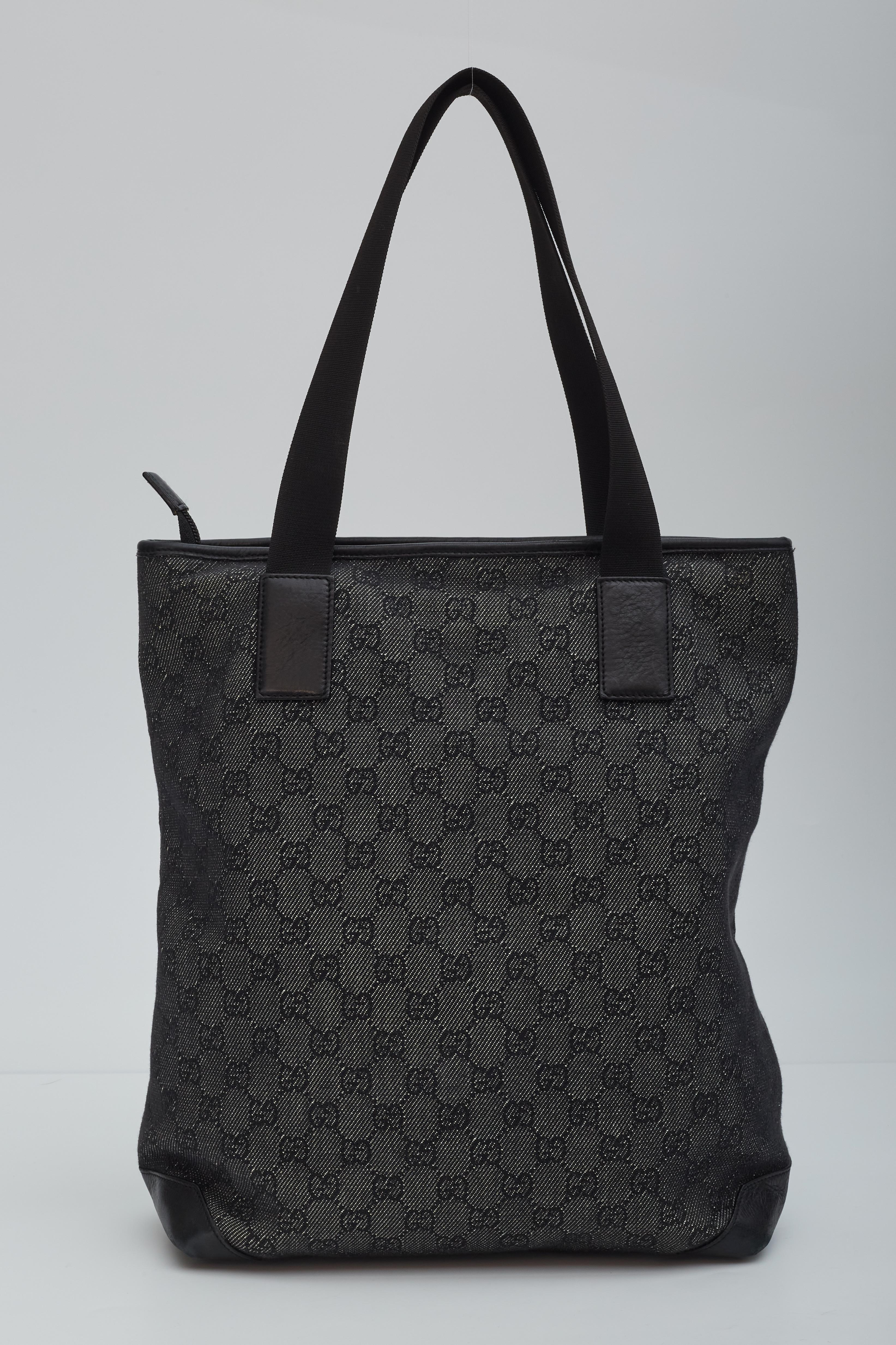This bag is constructed of classic black Gucci GG monogram on canvas. The bag features smooth black leather trim, including base corners, a large external zipper pocket, and anchors that secure black nylon shoulder straps. The top zipper opens to a