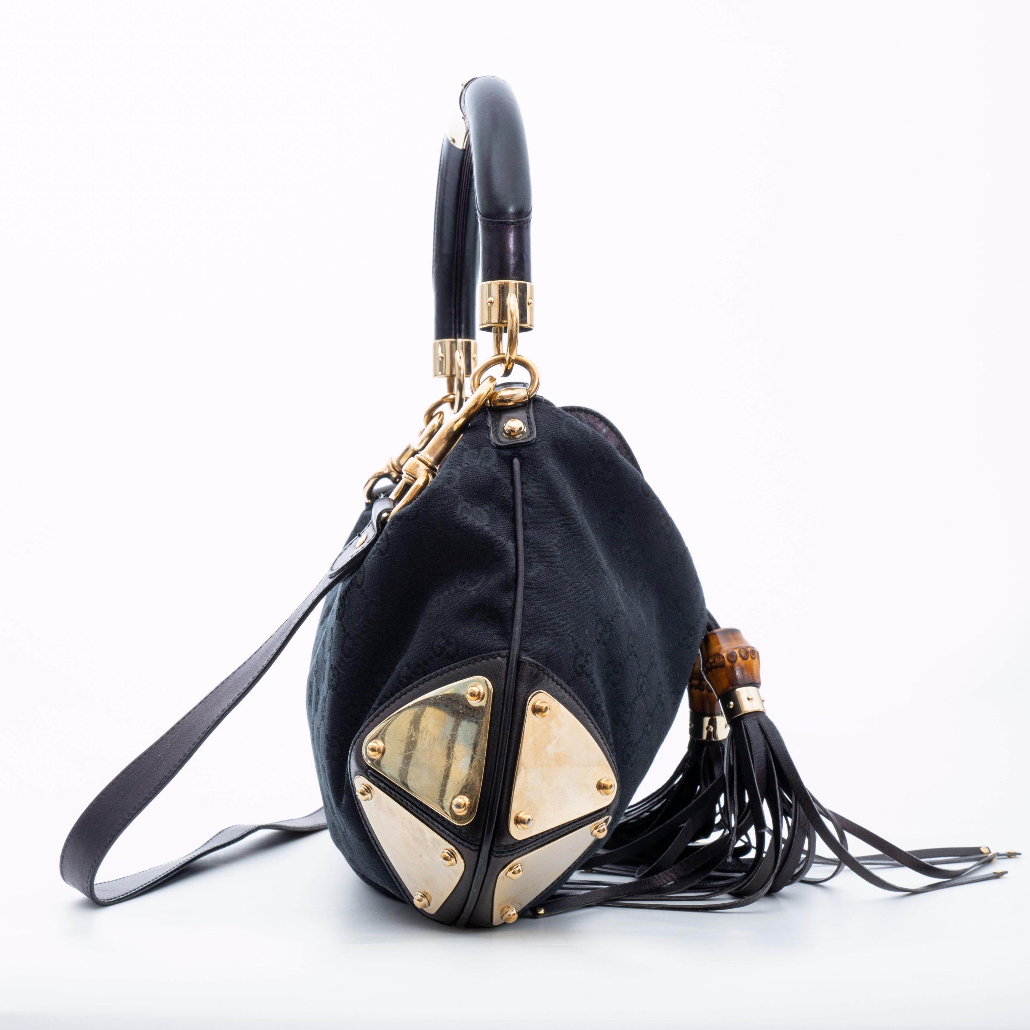La borsa è realizzata in tela nera con monogramma GG di Gucci. La borsa è dotata di un manico superiore in pelle nera rinforzato, arcuato e arrotolato con una placca dorata, anelli dorati lucidi e placche agli angoli laterali inferiori, con una