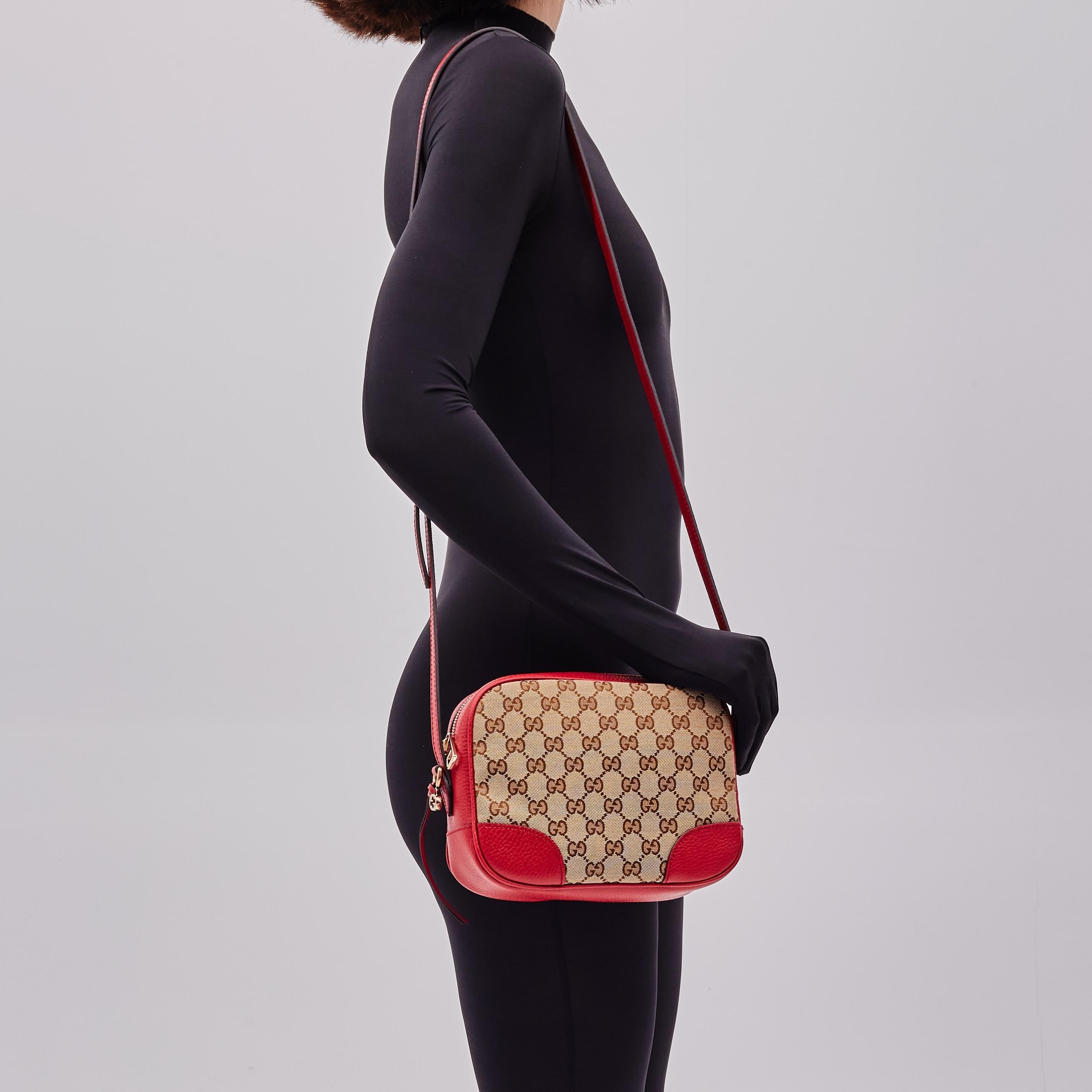 This Gucci crossbody bag is made of original brown and beige monogram printed canvas with red leather finishes. The bag features light-gold hardware, an adjustable shoulder strap, a GG charm and top zip closure with double zipper tabs. The zipper