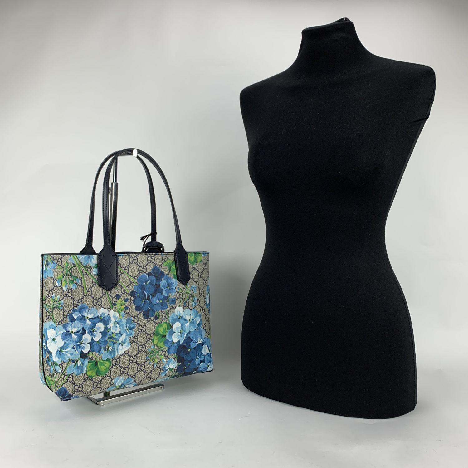 Beautiful Gucci reversible tote bag. The bag features a GG monogram Supreme canvas with Blooms print. on one side and blue leather on the other side. Open top. No interior pockets. Removable ID tag. Double handles. 'Gucci - Made in italy' engraved