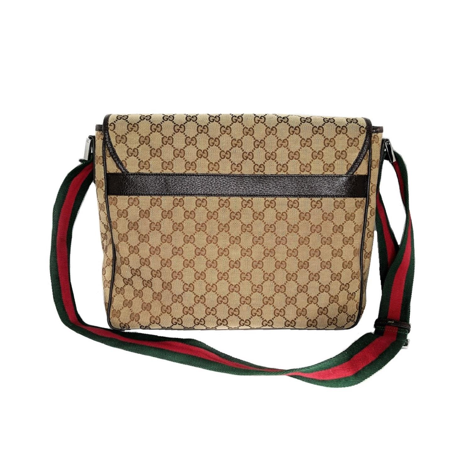 This stylish messenger bag is crafted of ebony on beige monogram canvas. It features a red and green striped nylon cross-body strap, gunmetal hardware, and dark brown leather trim. The flap opens to a brown fabric interior with zipper and patch