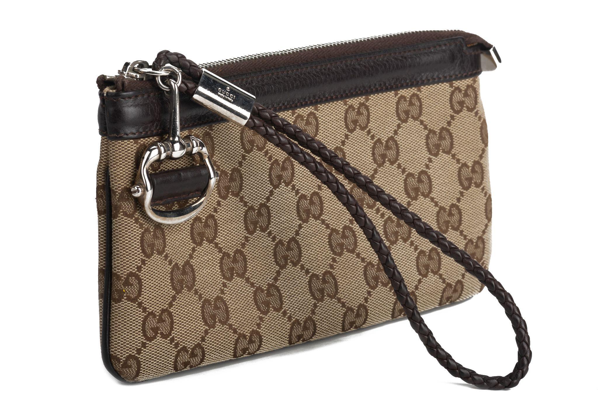 Gucci Monogram wrist wallet. The purse is made of fabric and has the tradition G monogram pattern. It comes with a wrist band and the zip to close it has a typical horse bit charm. The interior includes several card compartments. The piece comes