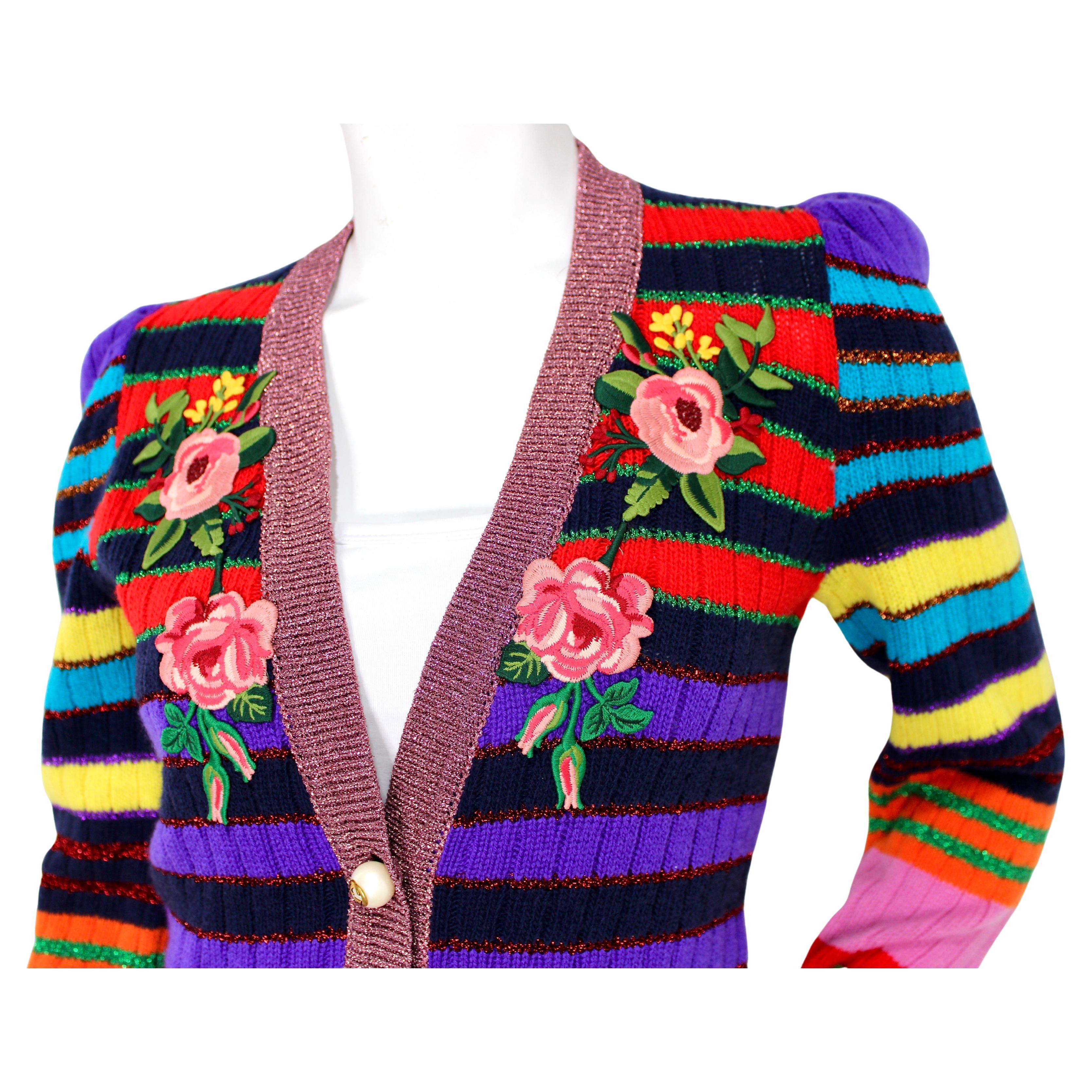 Le cardigan en maille à rayures multicolores et appliques florales de Gucci est une pièce vibrante et luxueuse qui allie harmonieusement un design ludique à un savoir-faire sophistiqué. Fabrice en tricot de haute qualité, ce cardigan présente des