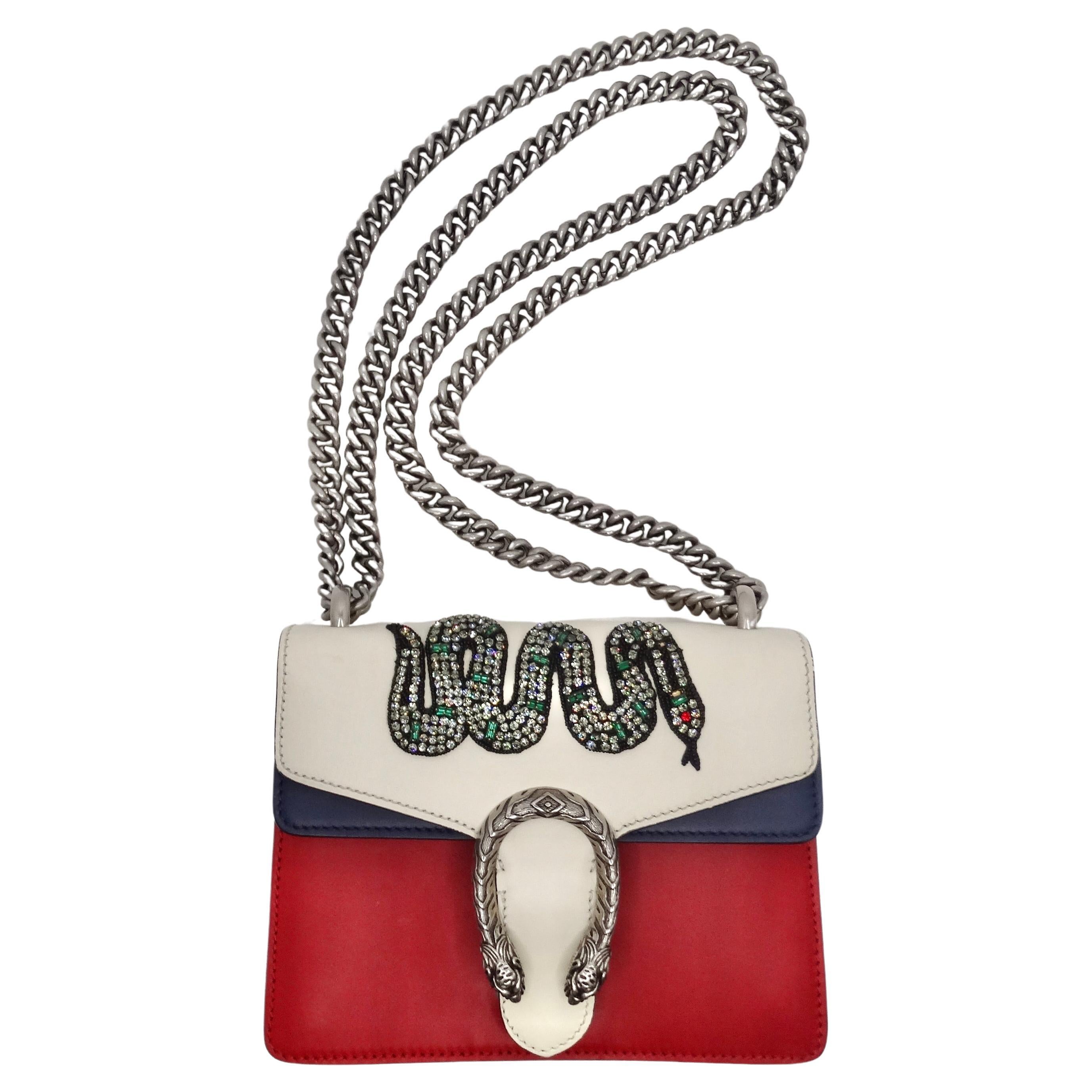 Introducing the Gucci Multicolor Leather Mini Crystal Snake Embroidered Dionysus Bag – a stunning fusion of artistry and luxury that makes an unforgettable statement. Crafted from red, white, and navy blue leather, this handbag is adorned with an
