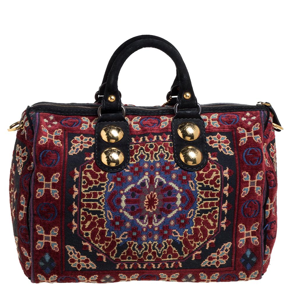 Crafted from multicolor tapestry fabric and leather, this Gucci Babouska Boston bag has two rolled top handles and a spacious fabric interior. It has been adorned with gold-tone studs and a logo detailed heart charm and comes equipped with