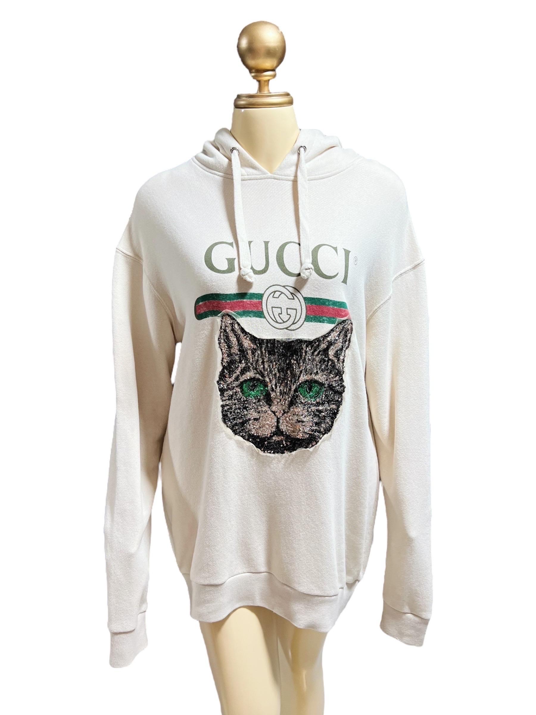 This relaxed Gucci hoodie showcases a printed vintage-effect logo across the chest and features the new season's Mystic Cat motif, embellished with shimmering sequins. It includes a drawstring hood, dropped shoulders, long sleeves, and ribbed hem