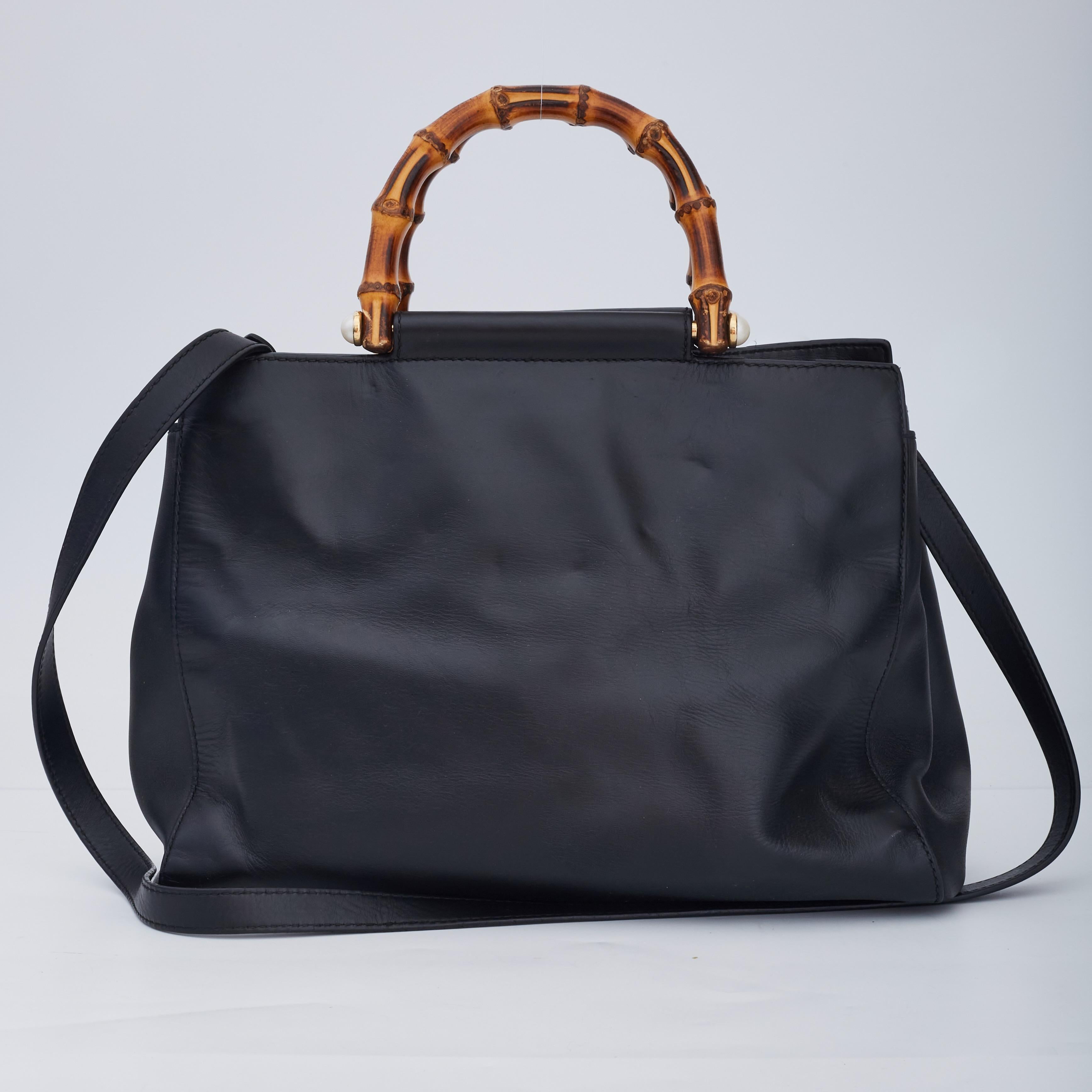 This bag is made of buttery soft nappa leather in black. The bag features looping bamboo handles with pearl details at the end of them, an optional leather shoulder strap and gold hardware. The top opens to a beige microfiber interior with zipper