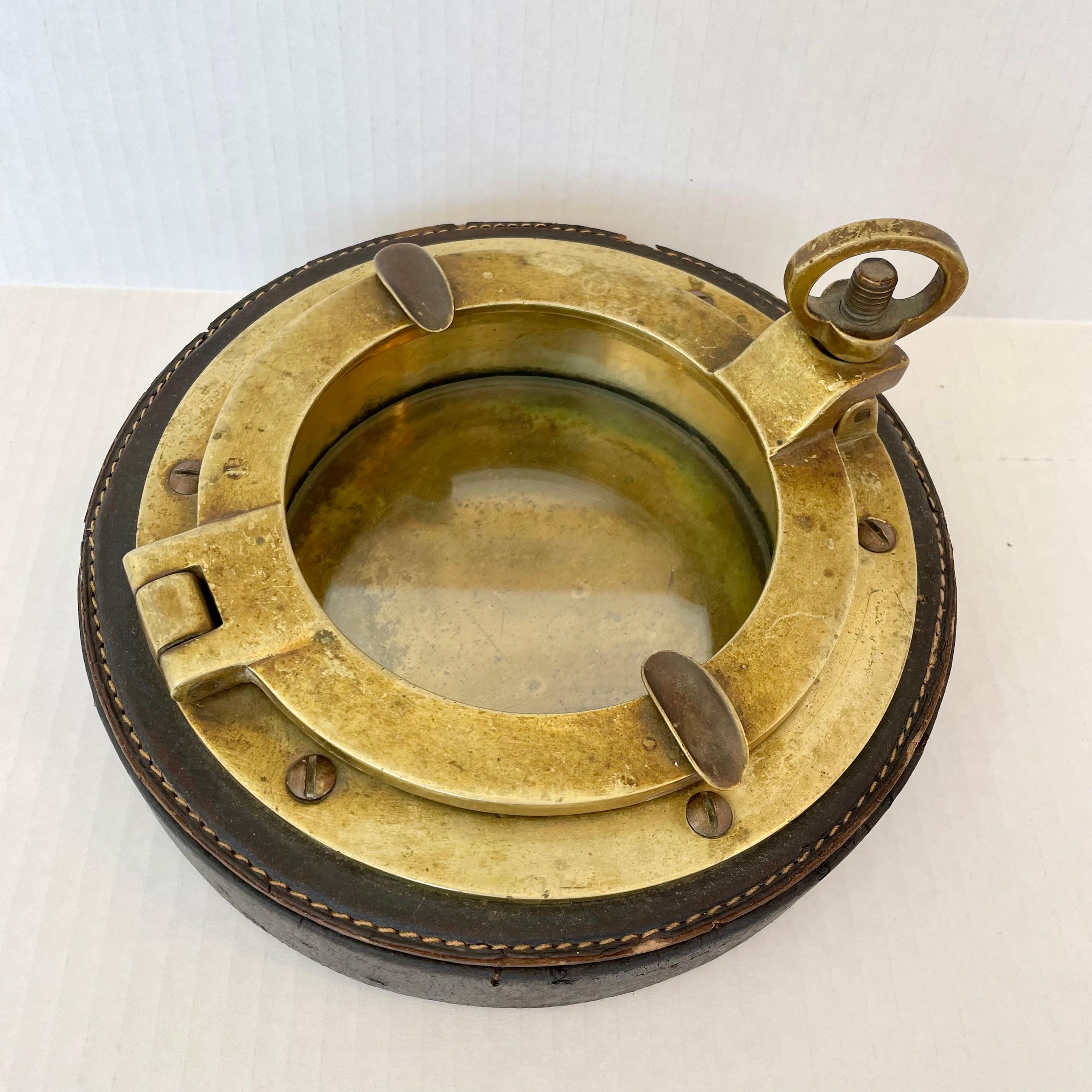 Impressive leather and brass ashtray by Gucci. Nautical theme with a working brass porthole that opens and closes to dump ashes. Leather frame. Heavy and substantial. Gucci stamp underneath. Large scale. Great piece of collectible Gucci design.