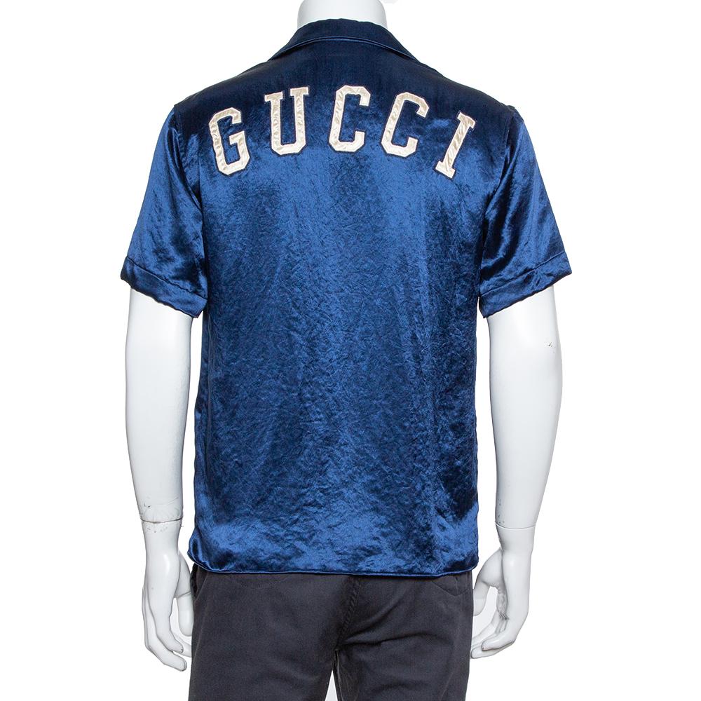 Walk with confidence and abundant style when you don this one of a kind bowling shirt from Gucci. Crafted from quality satin, it flaunts a navy blue with New York Yankee's patch in the front. The bowling shirt is styled with a collar, short sleeves,