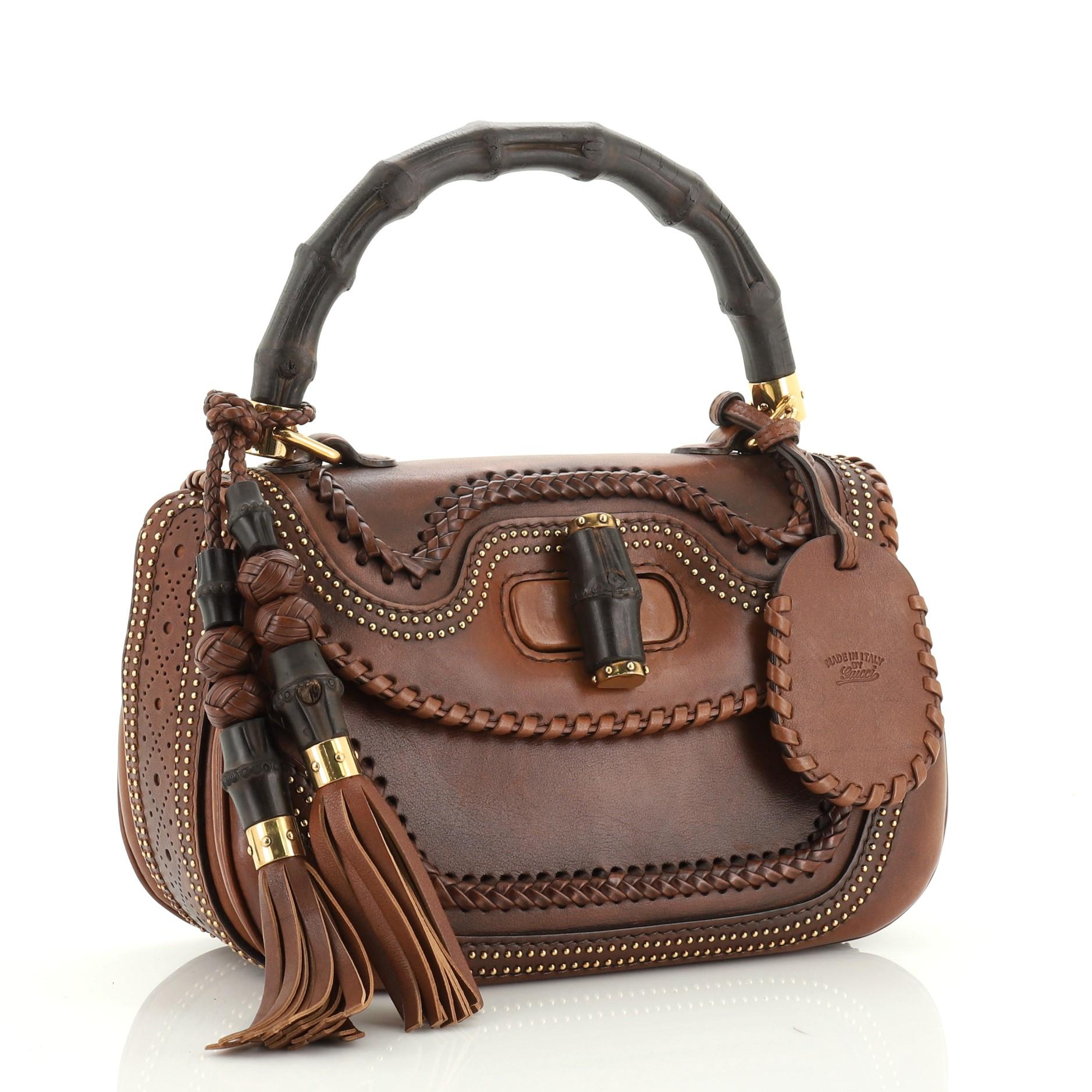 This Gucci New Bamboo Top Handle Bag Studded Leather Medium, crafted from brown leather, features a bamboo top handle, whipstitch and stud detailing, and gold-tone hardware. Its bamboo turn-lock closure opens to a brown microfiber interior with side