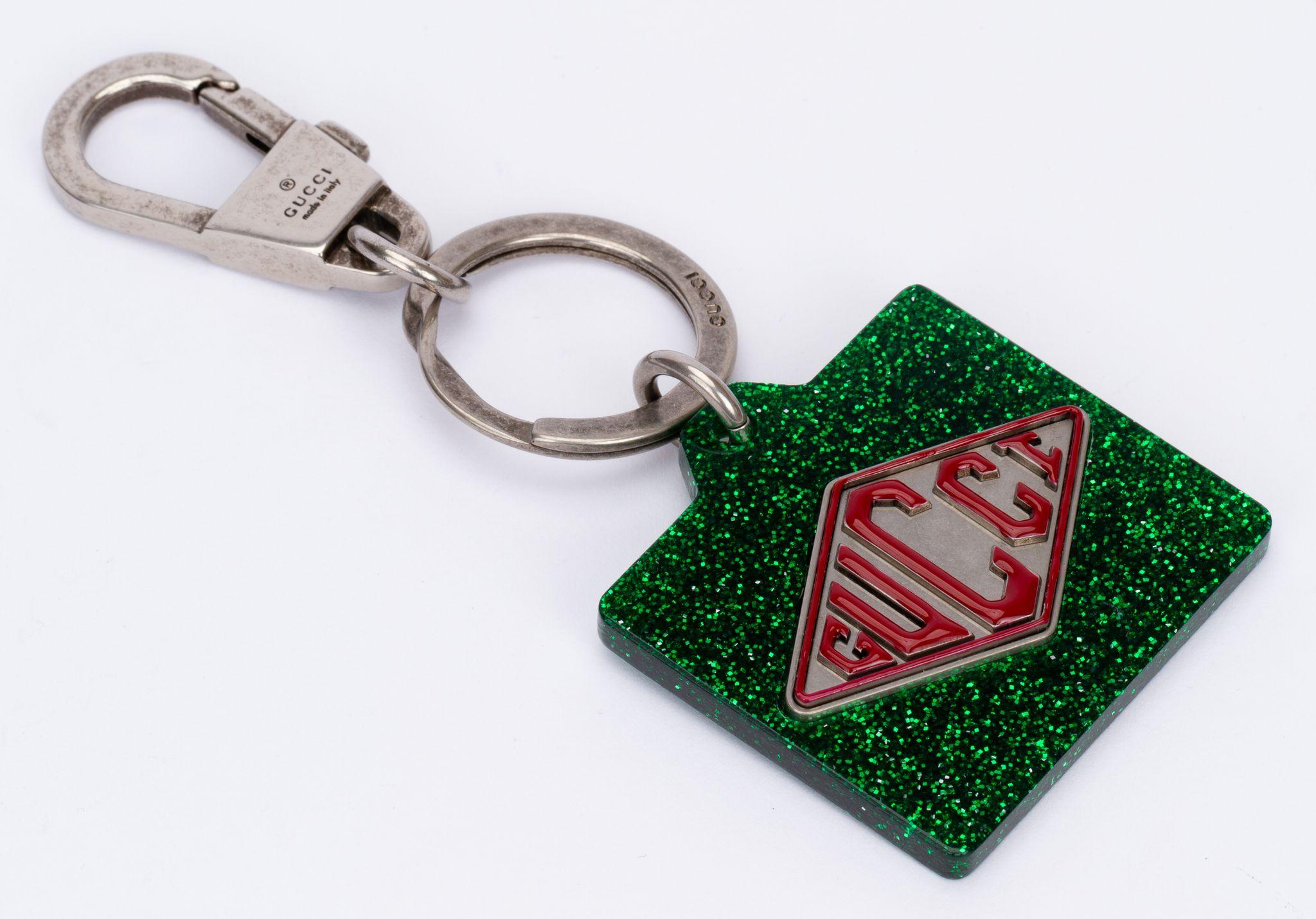 Gucci green glitter lucite charm key ring with a silver steel ring and clasp. In the middle of the charm is the Gucci logo written in red on white. The piece is brand new and comes with the tag and original box.