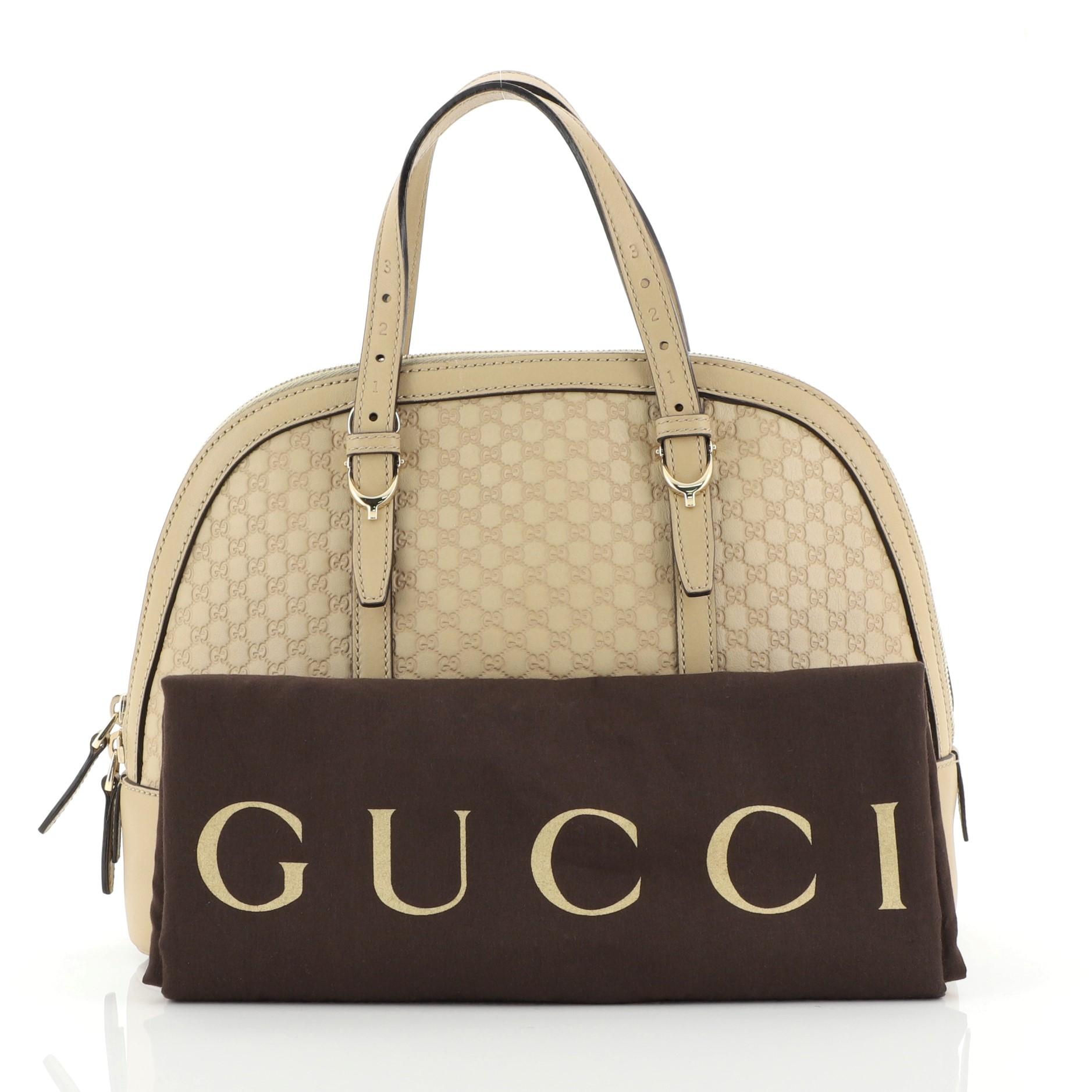 This Gucci Nice Top Handle Bag Microguccissima Leather Small, crafted in neutral microguccissima leather, features dual adjustable flat handles with spur details, protective base studs, and gold-tone hardware. Its two-way zip closure opens to a