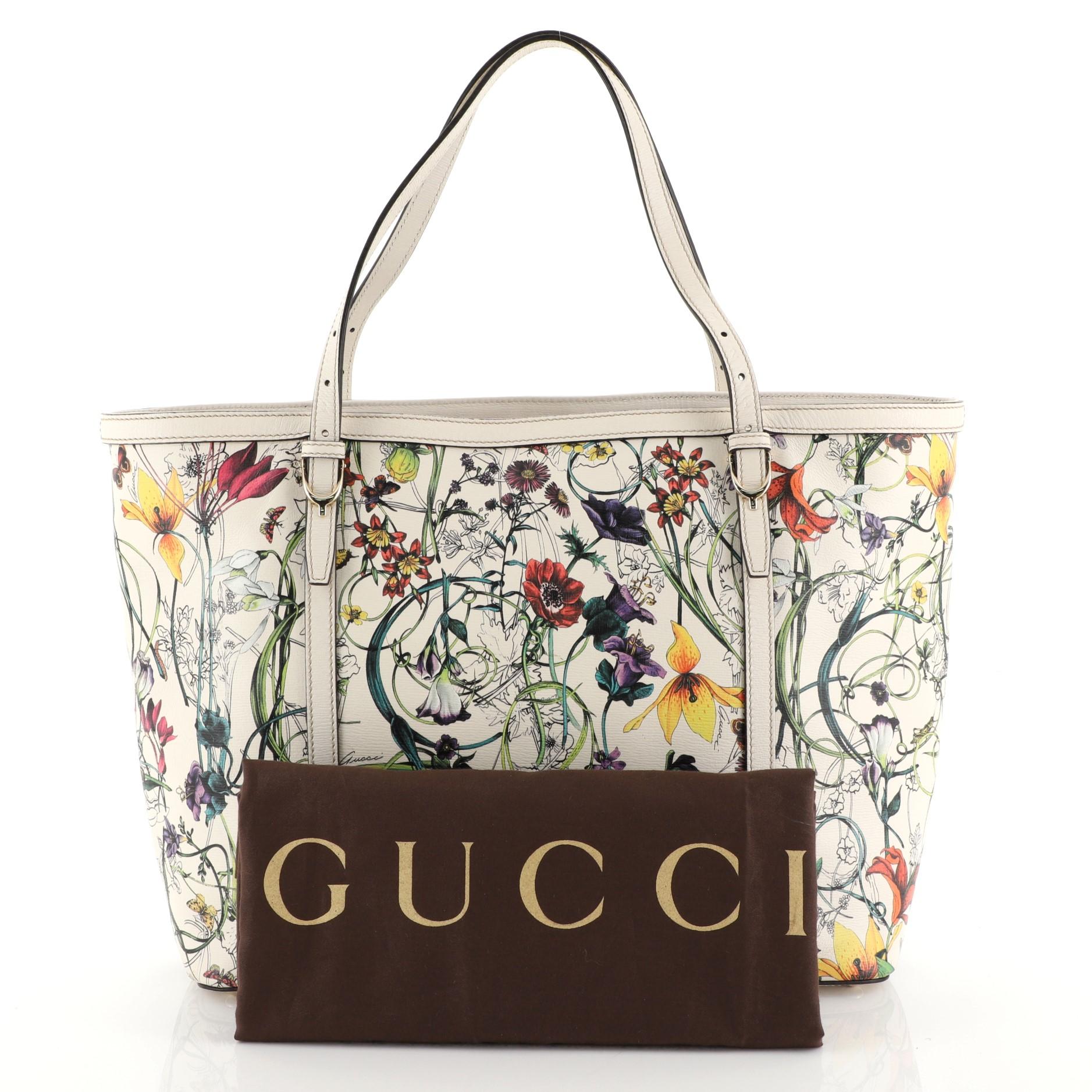This Gucci Nice Tote Floral Printed Leather Medium, crafted in white floral printed leather with white leather trims, features adjustable dual-flat handles with gold spur details and gold-tone hardware. Its hook closure opens to a purple fabric