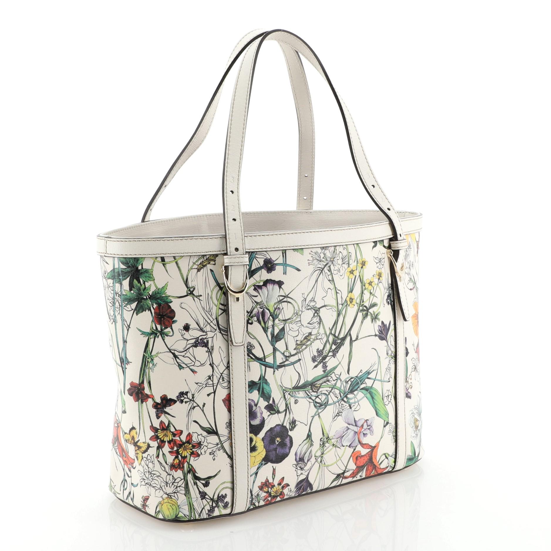 This Gucci Nice Tote Floral Printed Leather Small, crafted in white floral printed leather, features adjustable dual flat handles with spur details, leather trim and gold-tone hardware. Its hook closure opens to a purple fabric interior with side