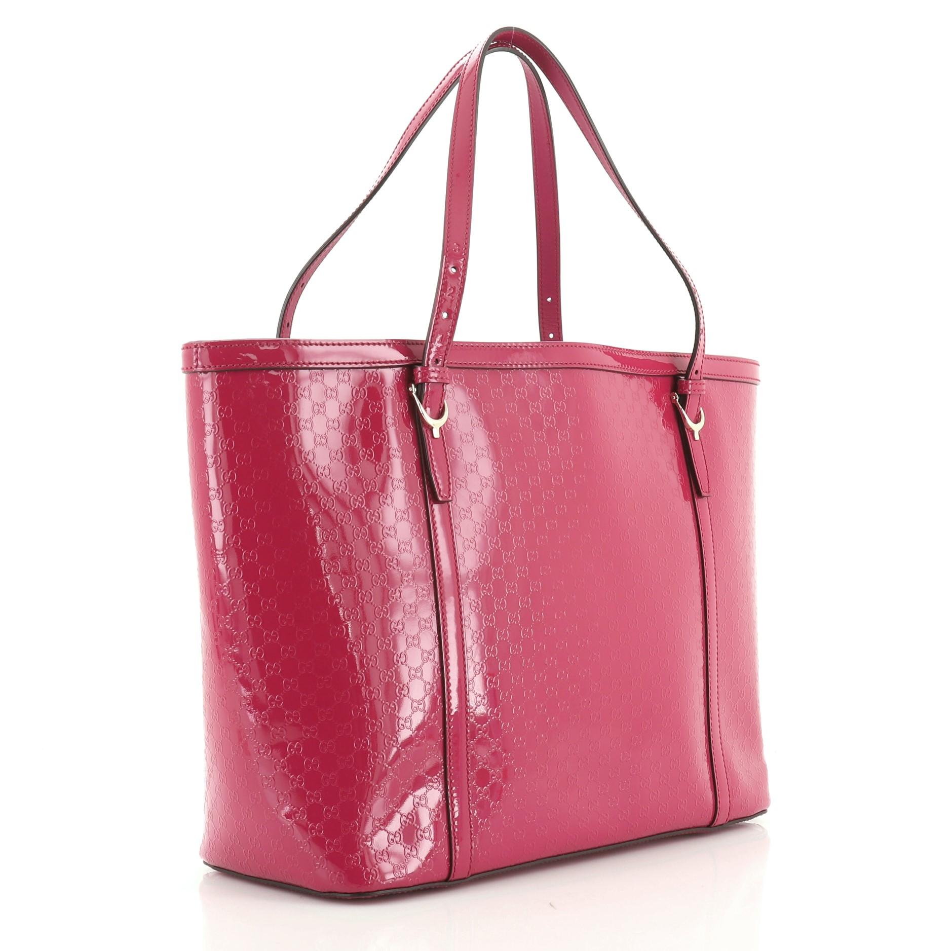 This Gucci Nice Tote Microguccissima Patent Medium, crafted in pink microguccissima patent leather, features dual adjustable flat handles, spur details, and gold-tone hardware. Its middle hook closure opens to a neutral fabric interior with zip and