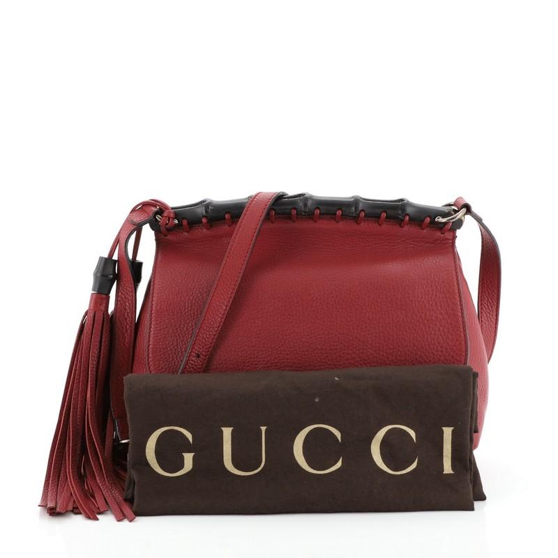 This Gucci Nouveau Crossbody Bag Leather Medium, crafted in red leather, features adjustable shoulder strap, lacquered bamboo bar across the top, bamboo tassel details, and bronze-tone hardware. Its bamboo closure opens to a neutral leather interior