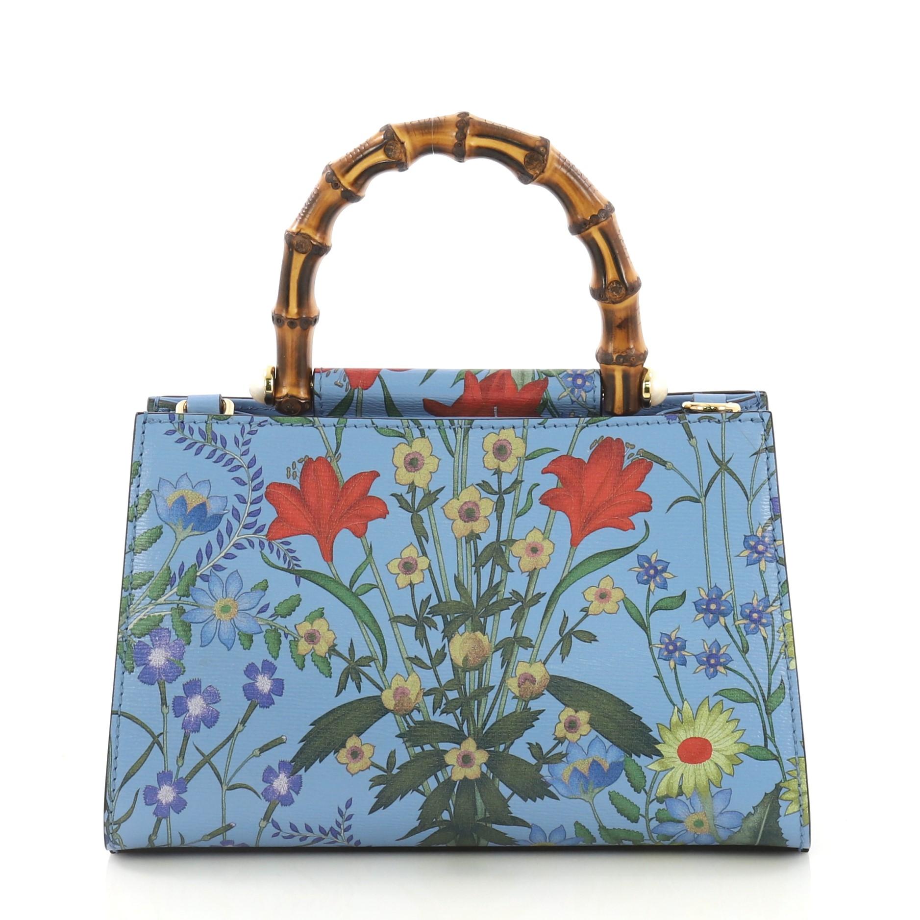 This Gucci Nymphaea Top Handle Bag Floral Print Leather Mini, crafted in floral print blue leather, features a bamboo handle with pearls and gold-tone hardware. Its magnetic snap closure opens to a beige microfiber interior with zip and slip