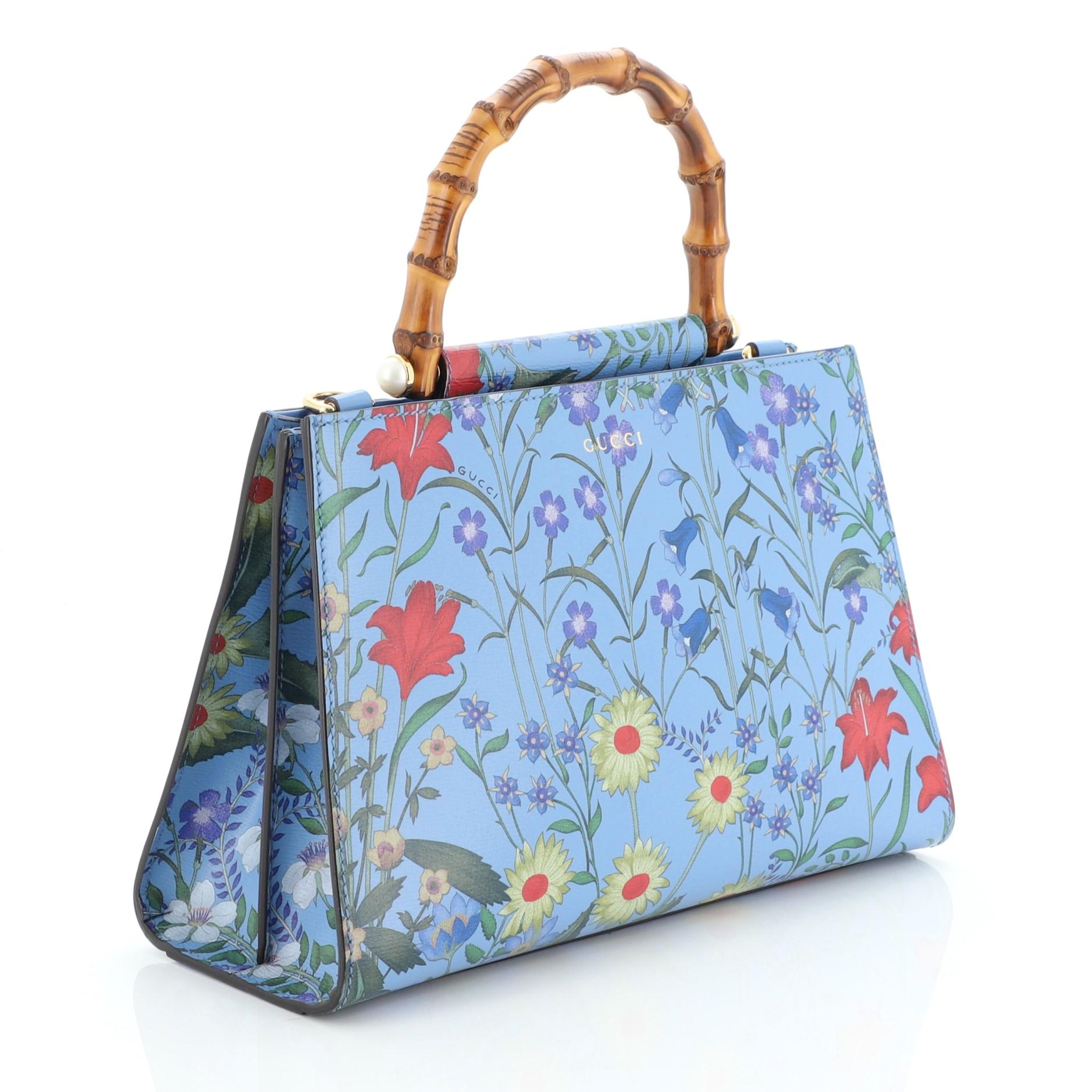 This Gucci Nymphaea Top Handle Bag Floral Printed Leather Small, crafted in printed floral blue leather, features a bamboo handle and gold-tone hardware. Its magnetic snap closure opens to a neutral microfiber interior with zip and slip pockets.
