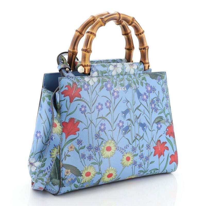This Gucci Nymphaea Tote Floral Printed Leather Small, crafted in floral print blue leather, features a bamboo handle with pearls and gold-tone hardware. Its magnetic snap closure opens to a neutral microfiber interior with zip and slip pockets.