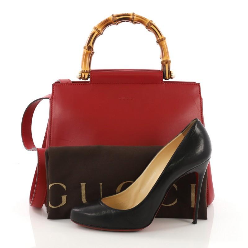 This Gucci Nymphaea Tote Leather Small, crafted in red leather, features dual top bamboo handles and gold-tone hardware. It opens to a beige fabric interior with zip and slip pockets. **Note: Shoe photographed is used as a sizing reference, and does