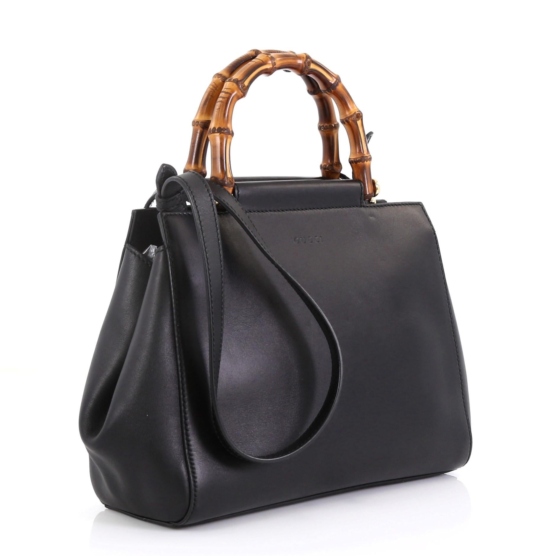 This Gucci Nymphaea Tote Leather Small, crafted in black leather, features a leather shoulder strap, bamboo handle with pearls, and gold-tone hardware accents. Its snap closure opens to a neutral microfiber interior with zip and slip pockets