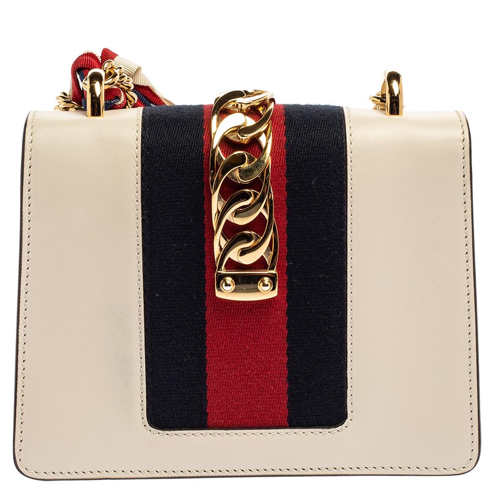 From the house of Gucci comes this gorgeous Sylvie shoulder bag that will perfectly complement all your outfits. It has been luxuriously crafted from off white leather and styled with a chain-web decorated flap and a gold-tone buckle lock to secure